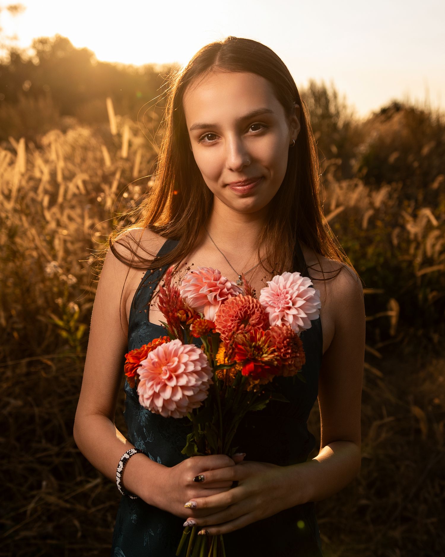 Person holding colorful dahlia flowers during golden hour sunset in a field.