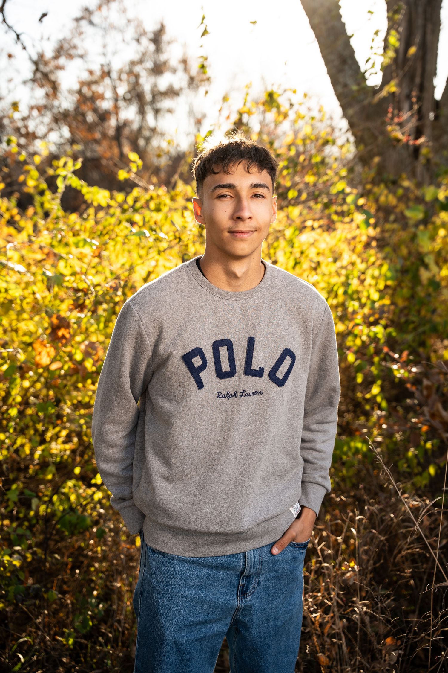 Person wearing gray Polo sweatshirt standing against golden autumn foliage.