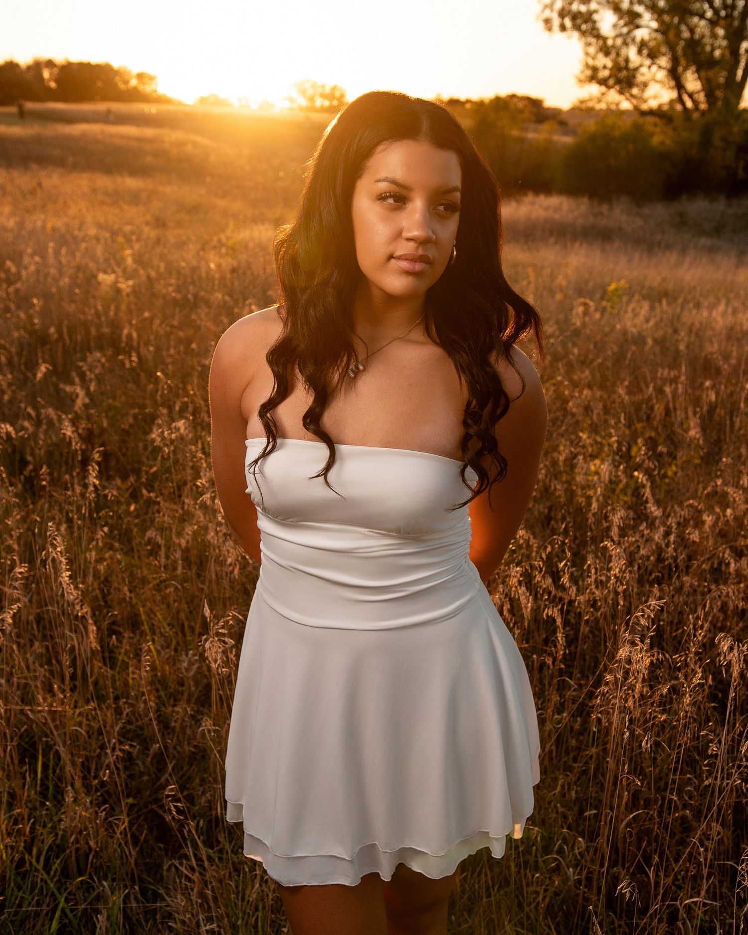 Woman in white dress standing in golden field at sunset.