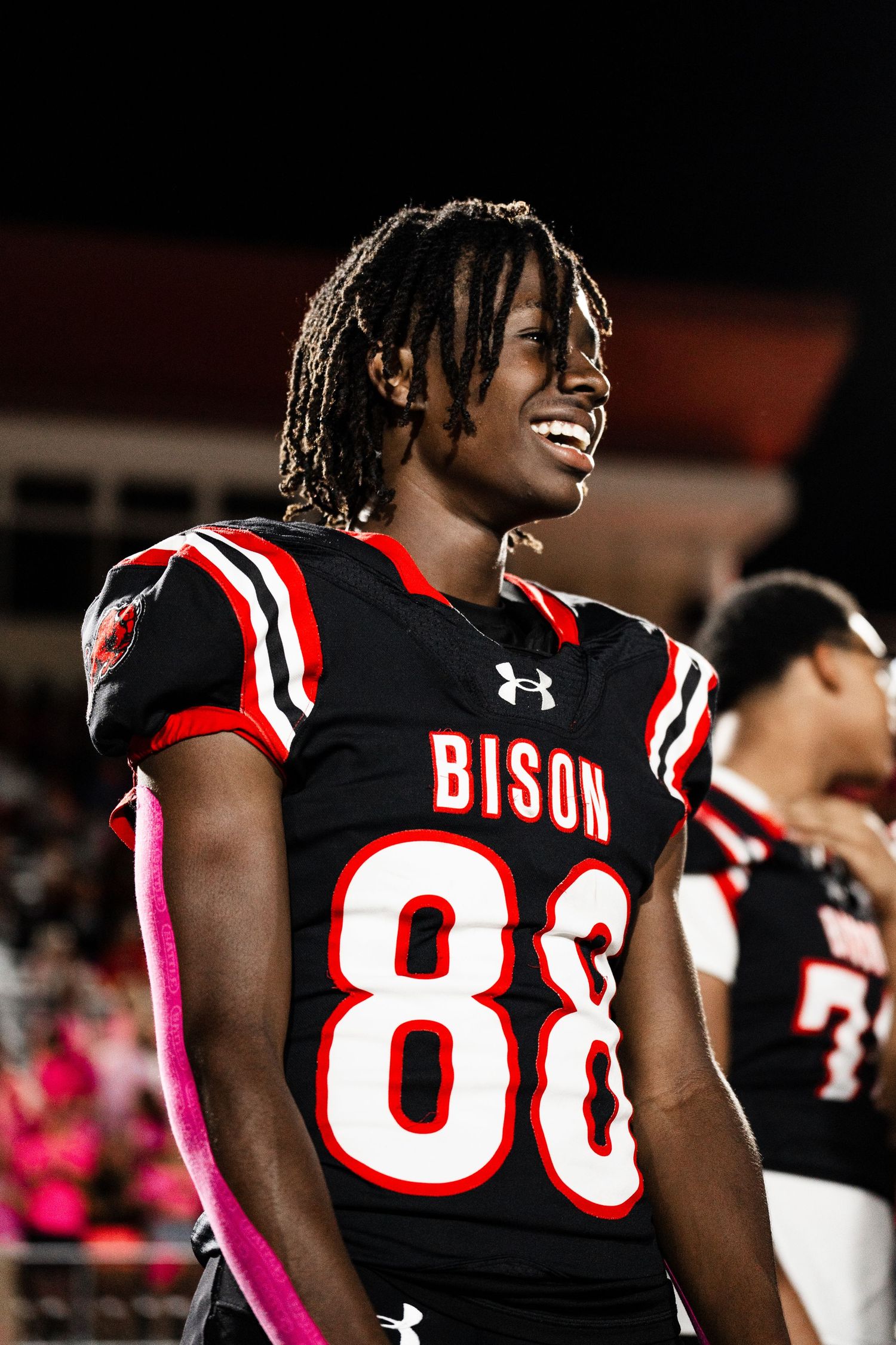 Smiling football players in black Bison jerseys with number 88 wearing pink accessories.
