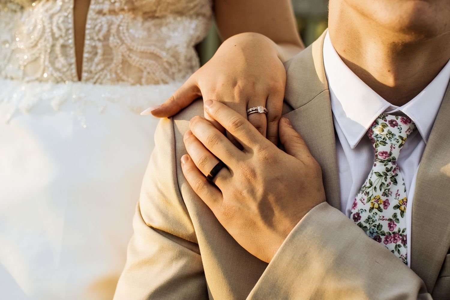 Close-up of bride and groom hands showing wedding rings, groom wearing floral tie.