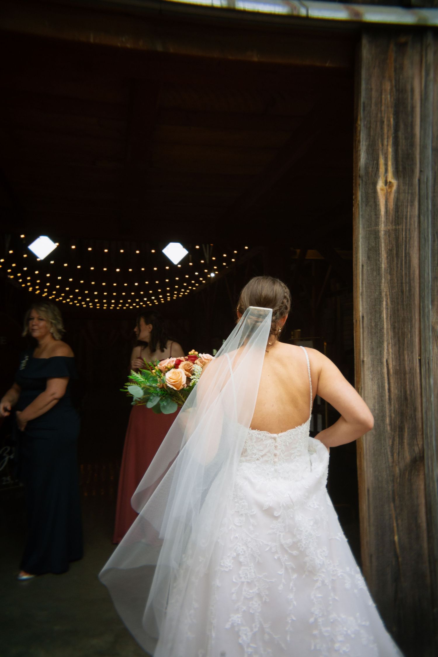 A bride in a white wedding dress and veil dances under twinkling string lights at an indoor reception venue.