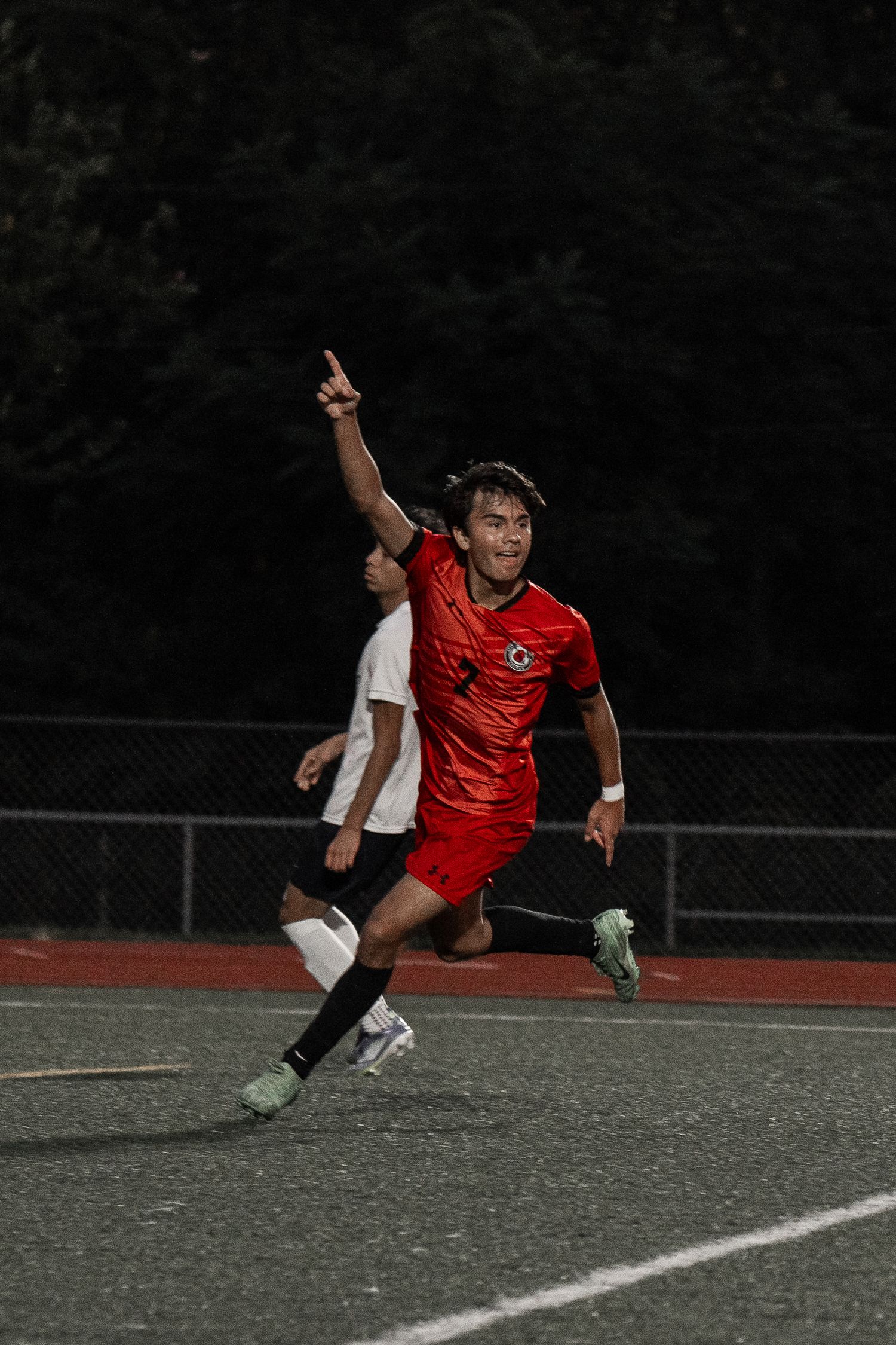 Soccer player in red uniform leaps dramatically during nighttime match.