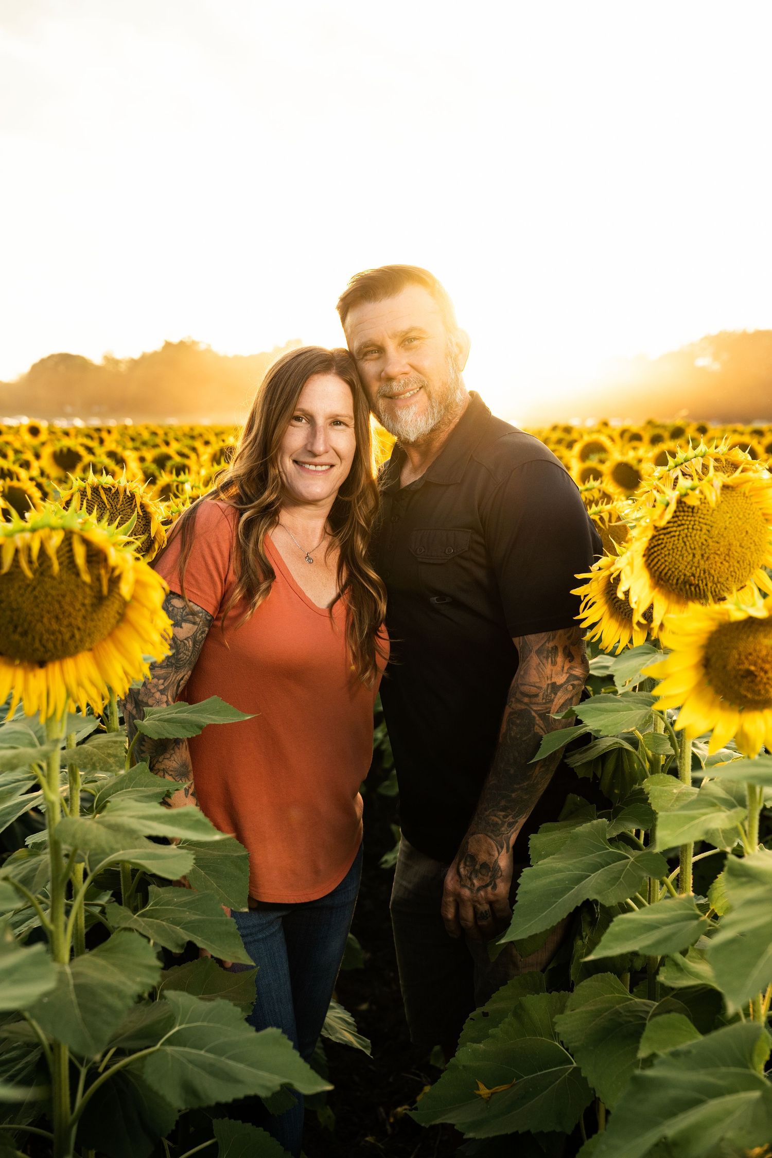 People share intimate moments among tall sunflowers during a warm sunset photoshoot.