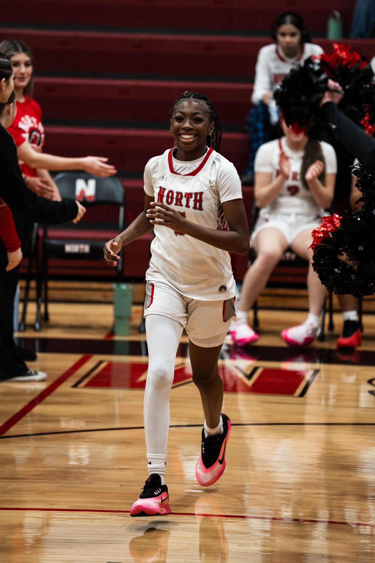 Basketball player in white uniform and pink shoes performs dynamic moves on the court during a game.