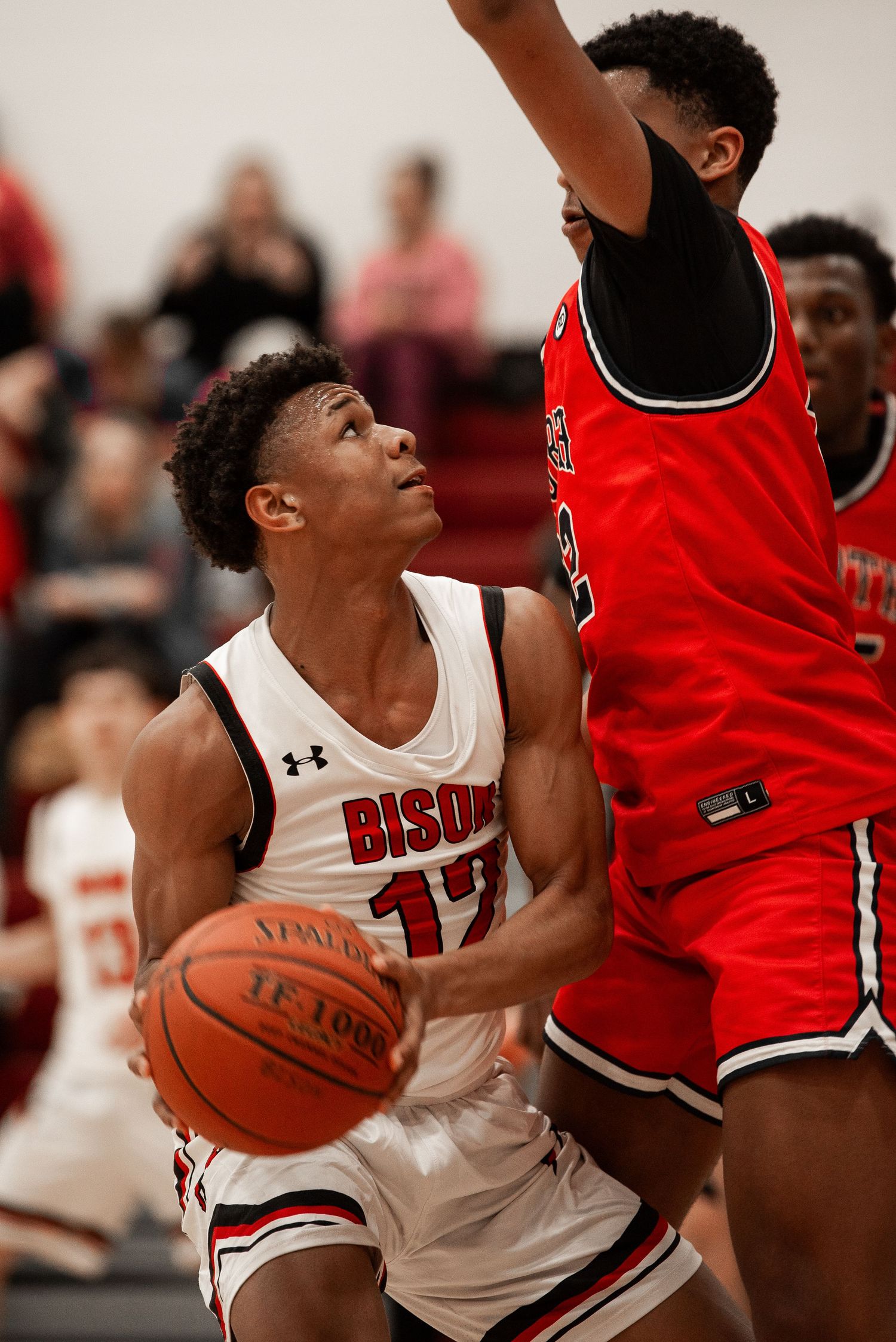 Basketball player in white jersey drives to the basket against defender in red during intense game action.