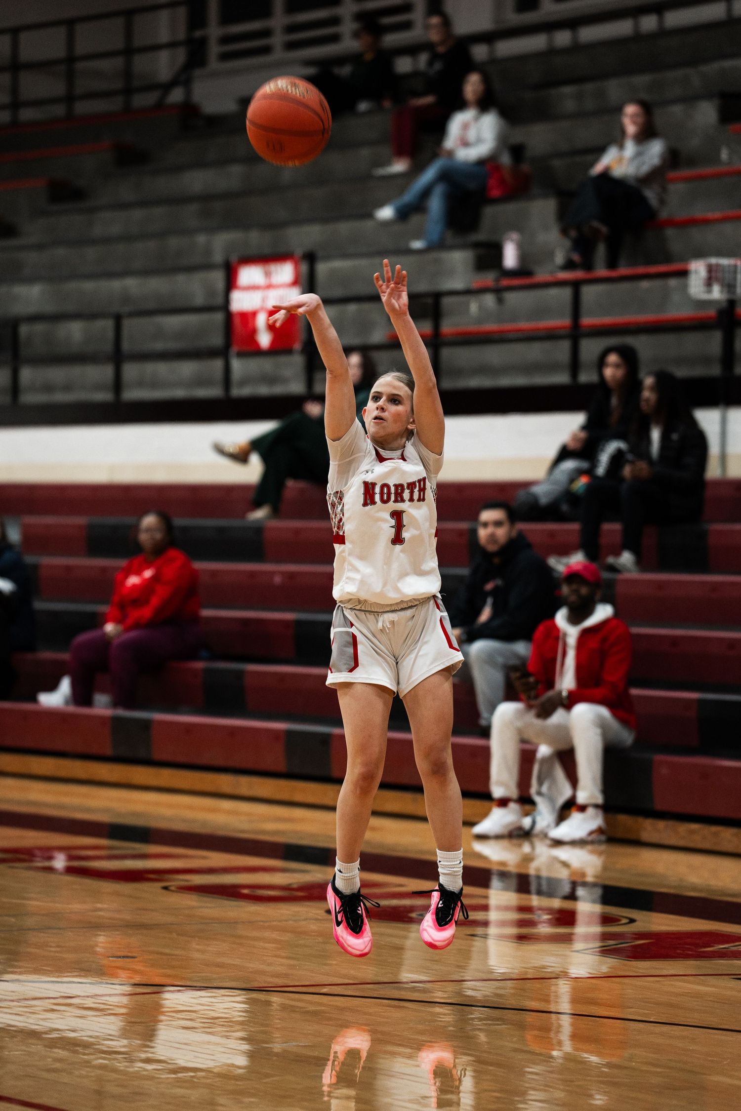 Player in white jersey jumps to shoot a basketball in a gymnasium setting.