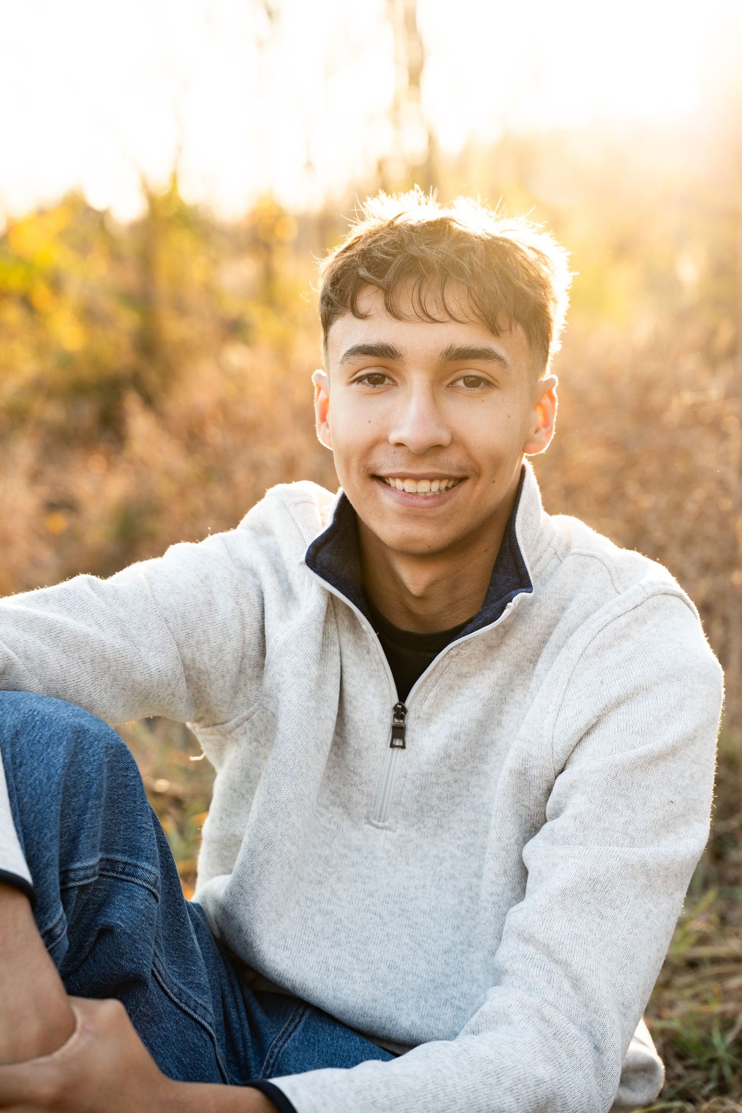 Person in gray quarter-zip sweater relaxing on ground during golden hour.
