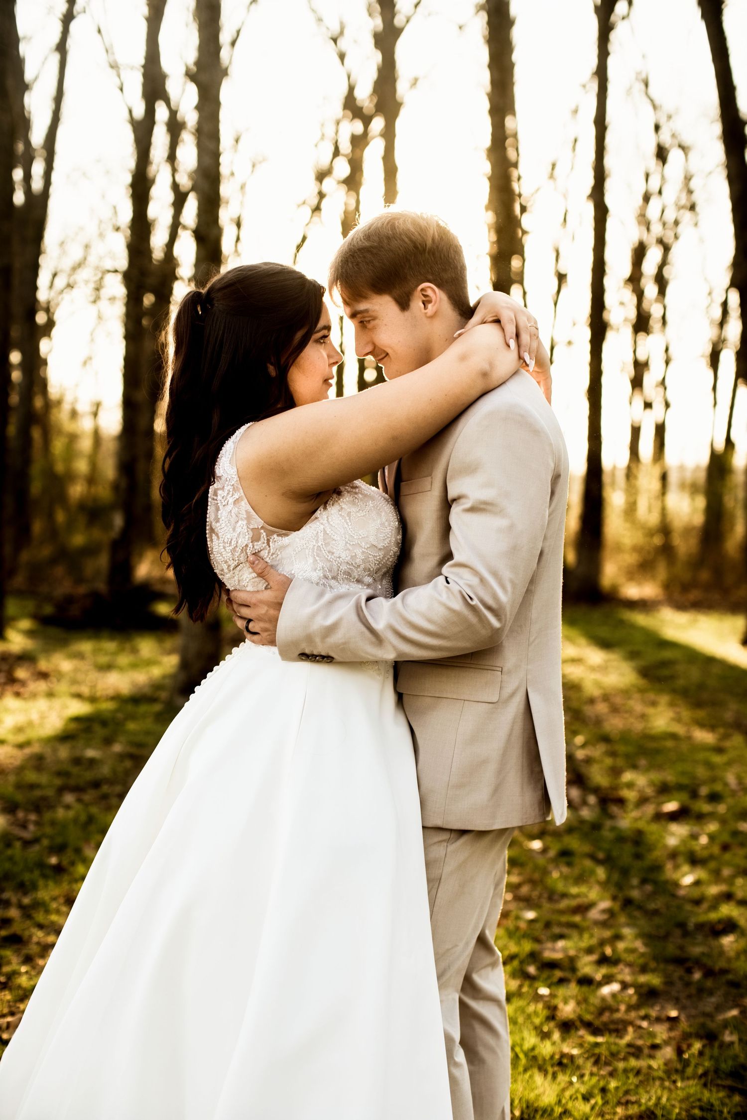 Bride and groom embracing face to face in a sunlit autumn forest setting.