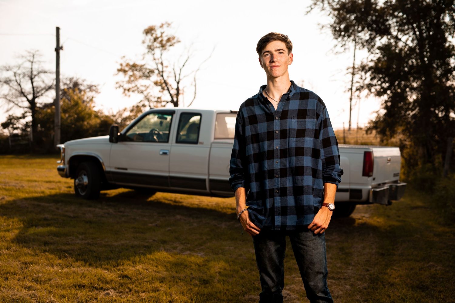 Rural outdoor photoshoot with pickup trucks in background during sunset.