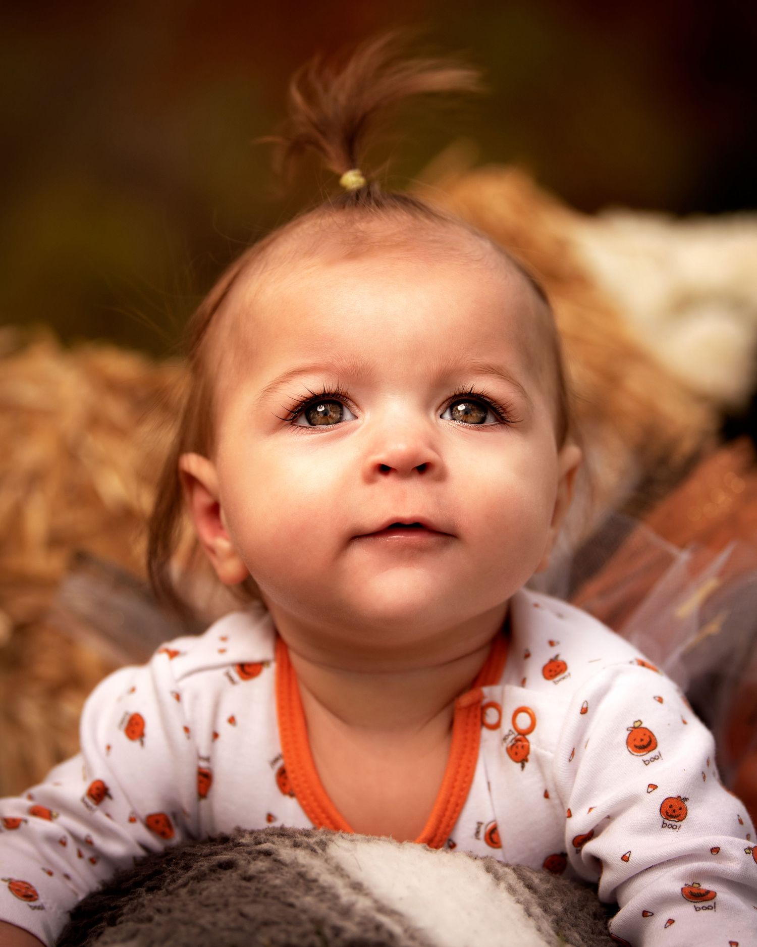 Baby wearing white and orange ladybug print outfit lying on soft blanket.