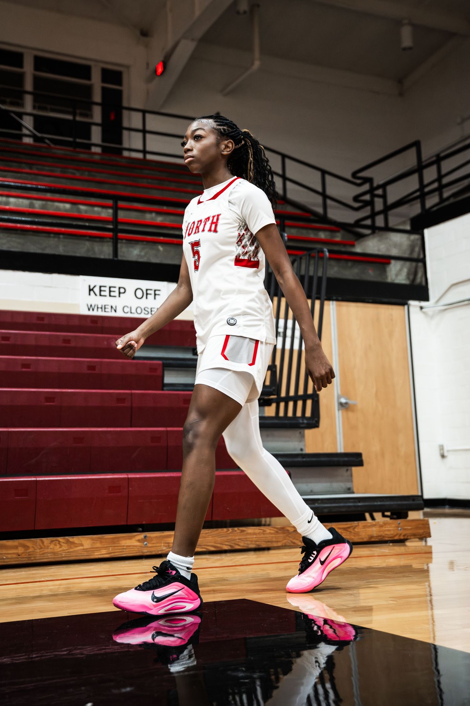 Close-up of pink and black basketball shoes on wooden gym floor.
