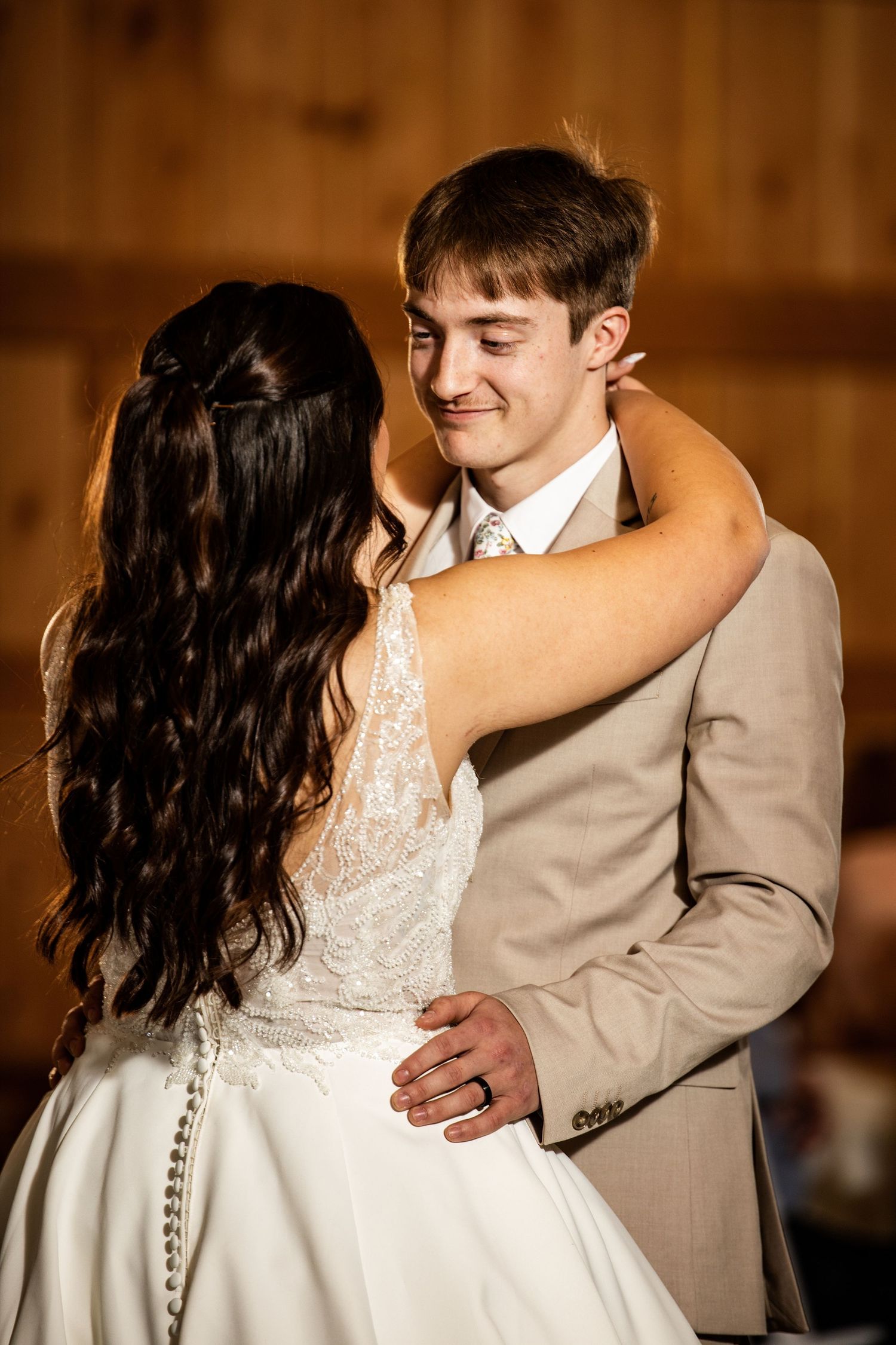 Groom smiling tenderly while sharing first dance with bride in a rustic barn.