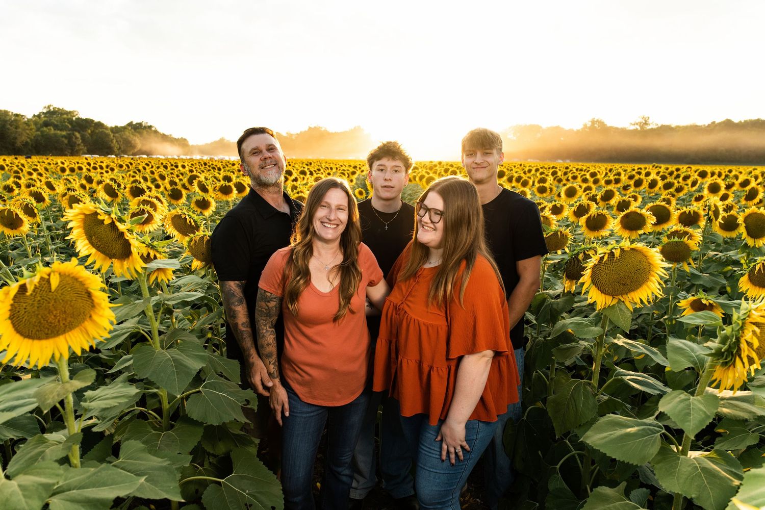 A couple poses together in a vibrant sunflower field at golden hour, creating a romantic autumn scene.