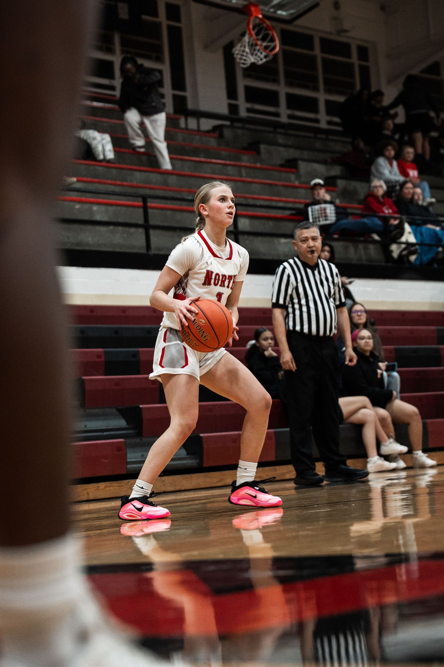 Basketball player in white uniform crouches low while dribbling during game play.