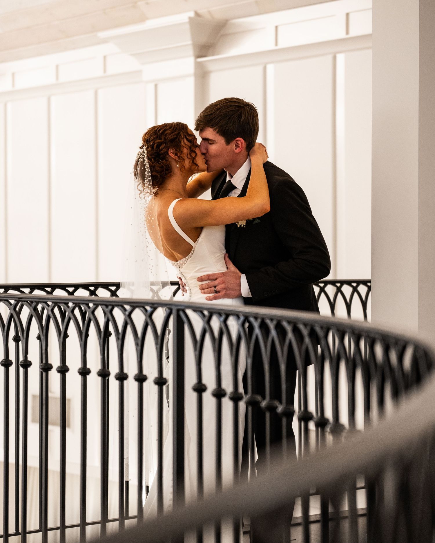 A romantic wedding couple sharing an intimate moment on a balcony with decorative iron railings.