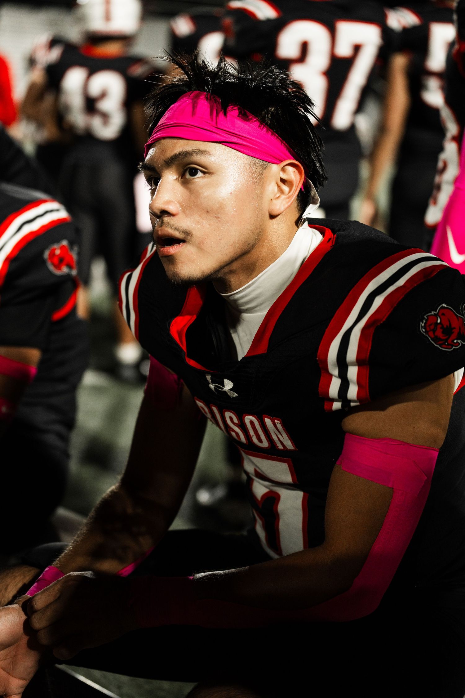 Close-up of football players wearing black Bison uniforms and pink headbands in dramatic lighting.