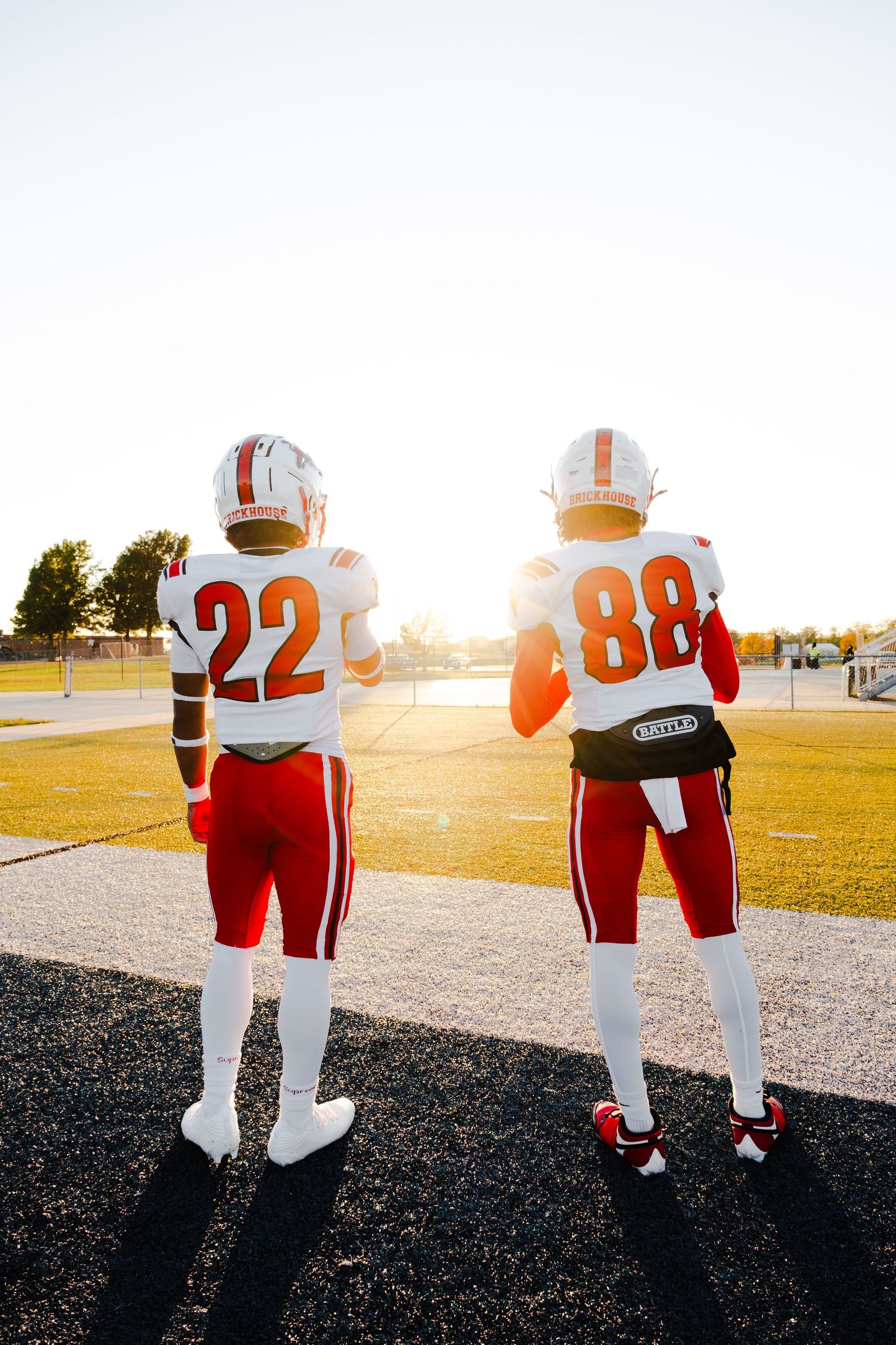 Football players in red and white jerseys photographed from behind during golden hour.