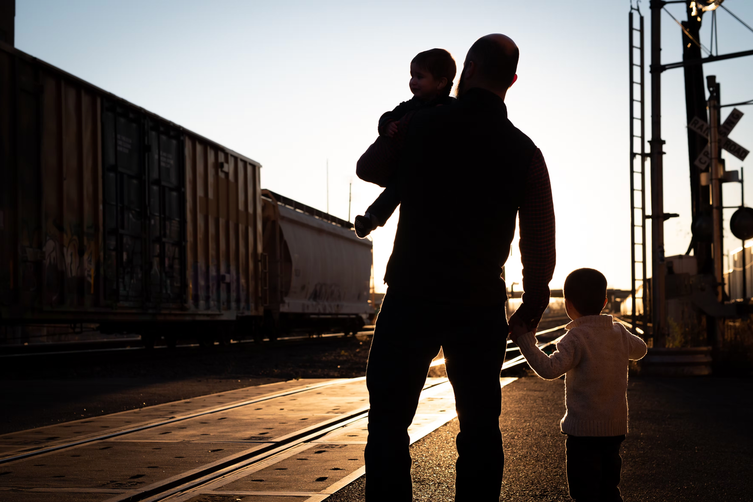 Silhouetted figures walk along a train track at sunset creating dramatic shadows and lighting.