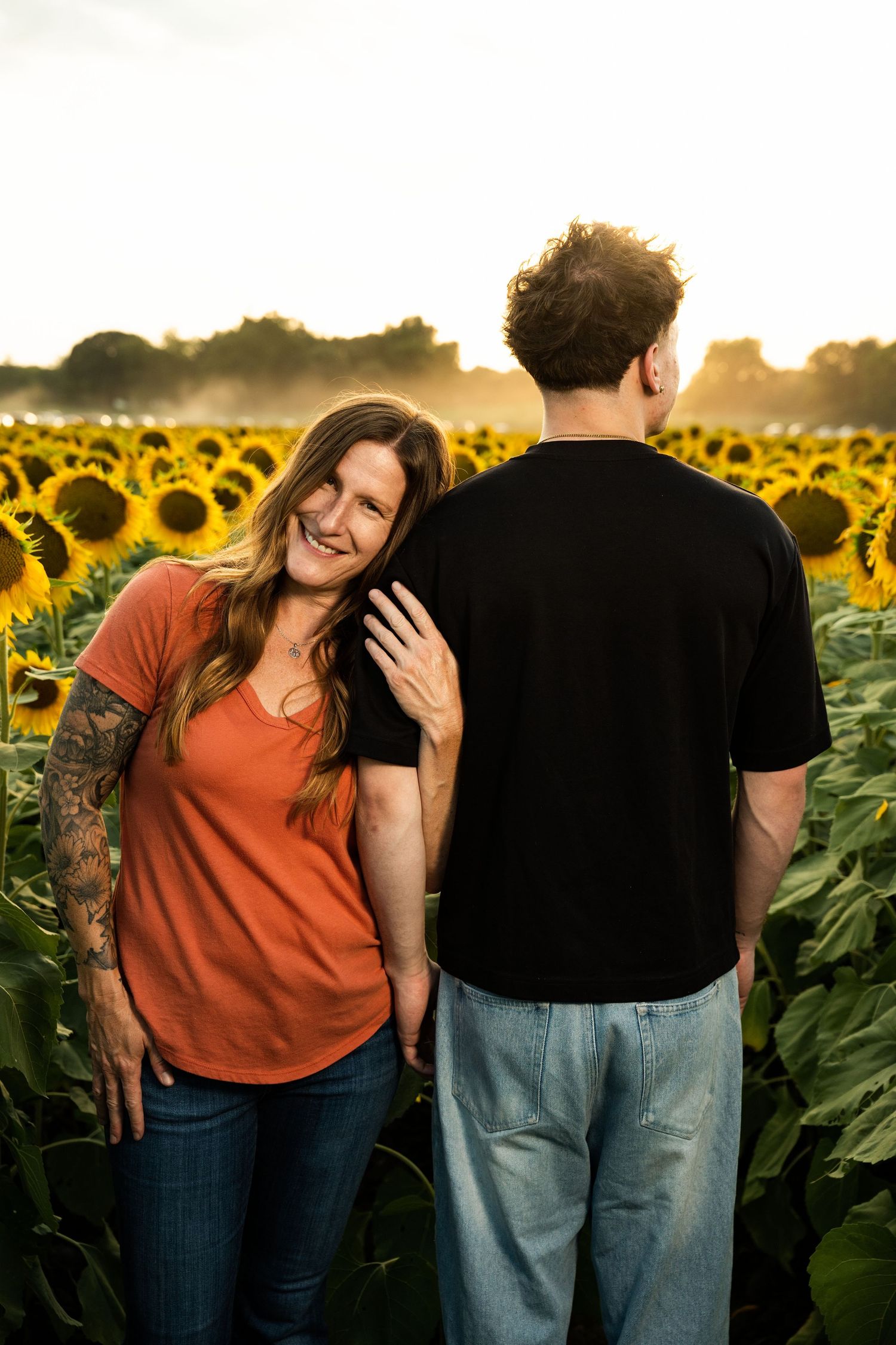 Candid moments captured between people in a sunflower field at sunset with warm golden lighting.