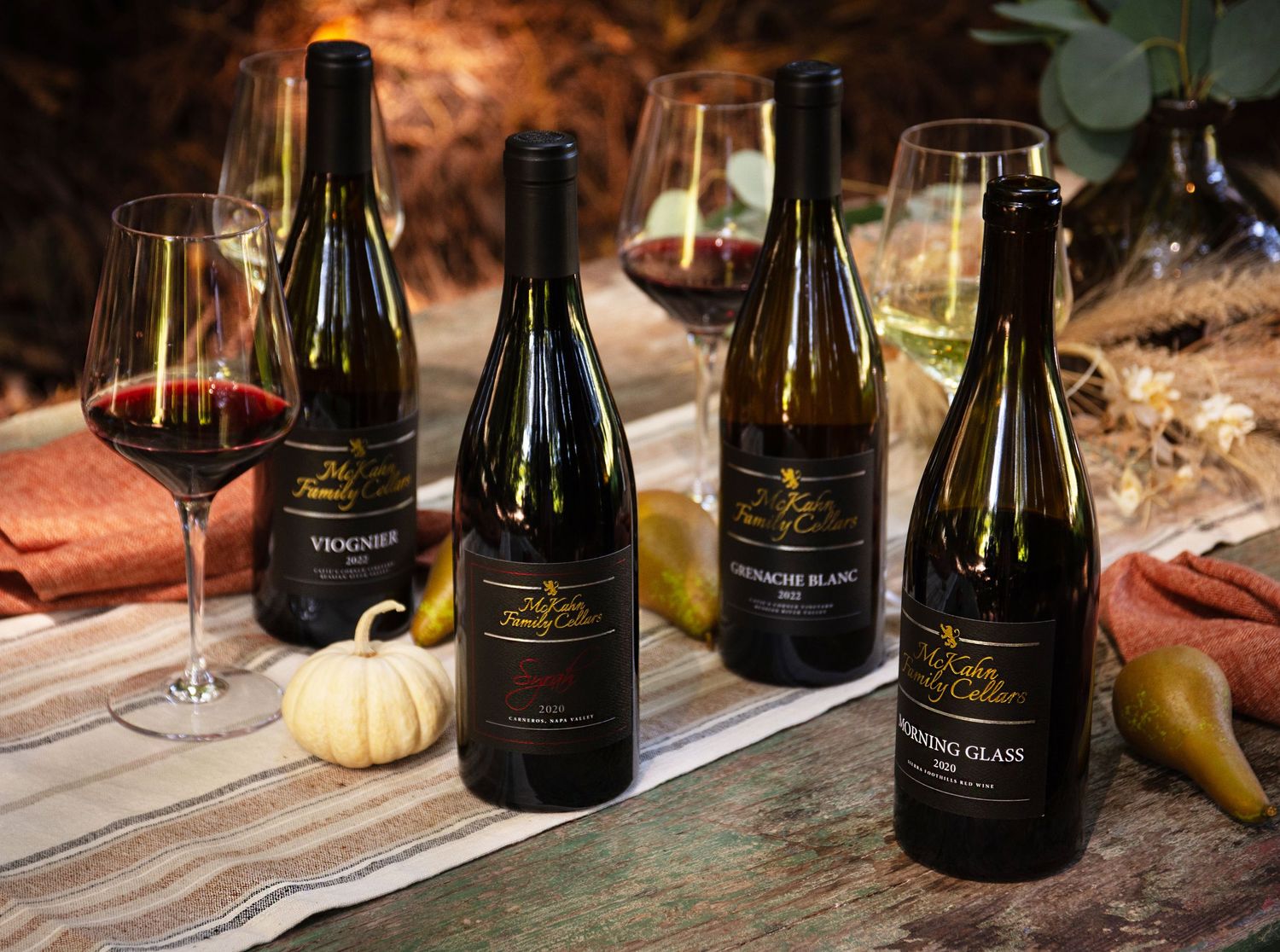 Four wine bottles including Viognier and Sauvignon Blanc varieties displayed on a rustic table with wine glasses and autumn decor.