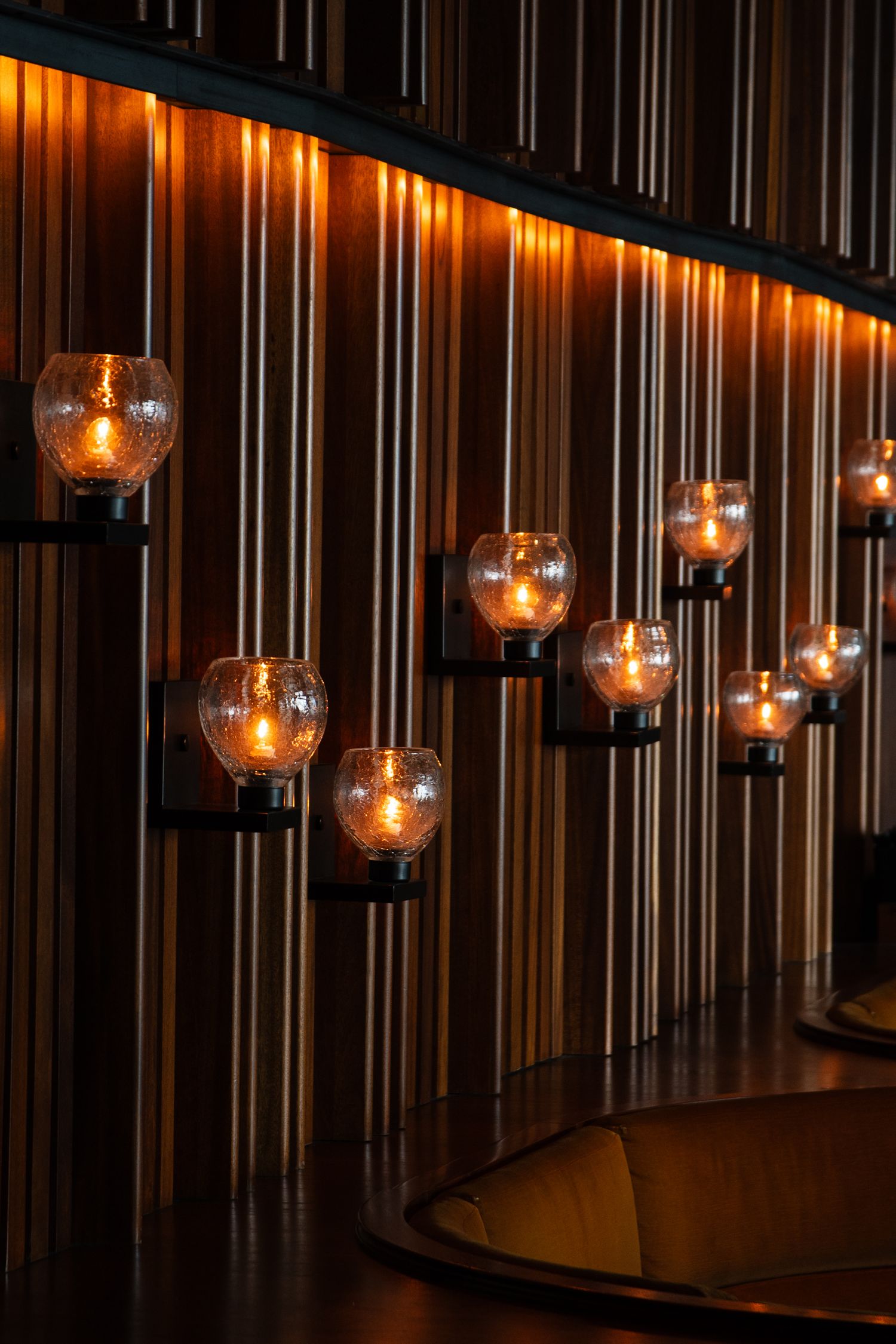 Row of illuminated glass pendant lights hanging from a dark wooden ceiling.