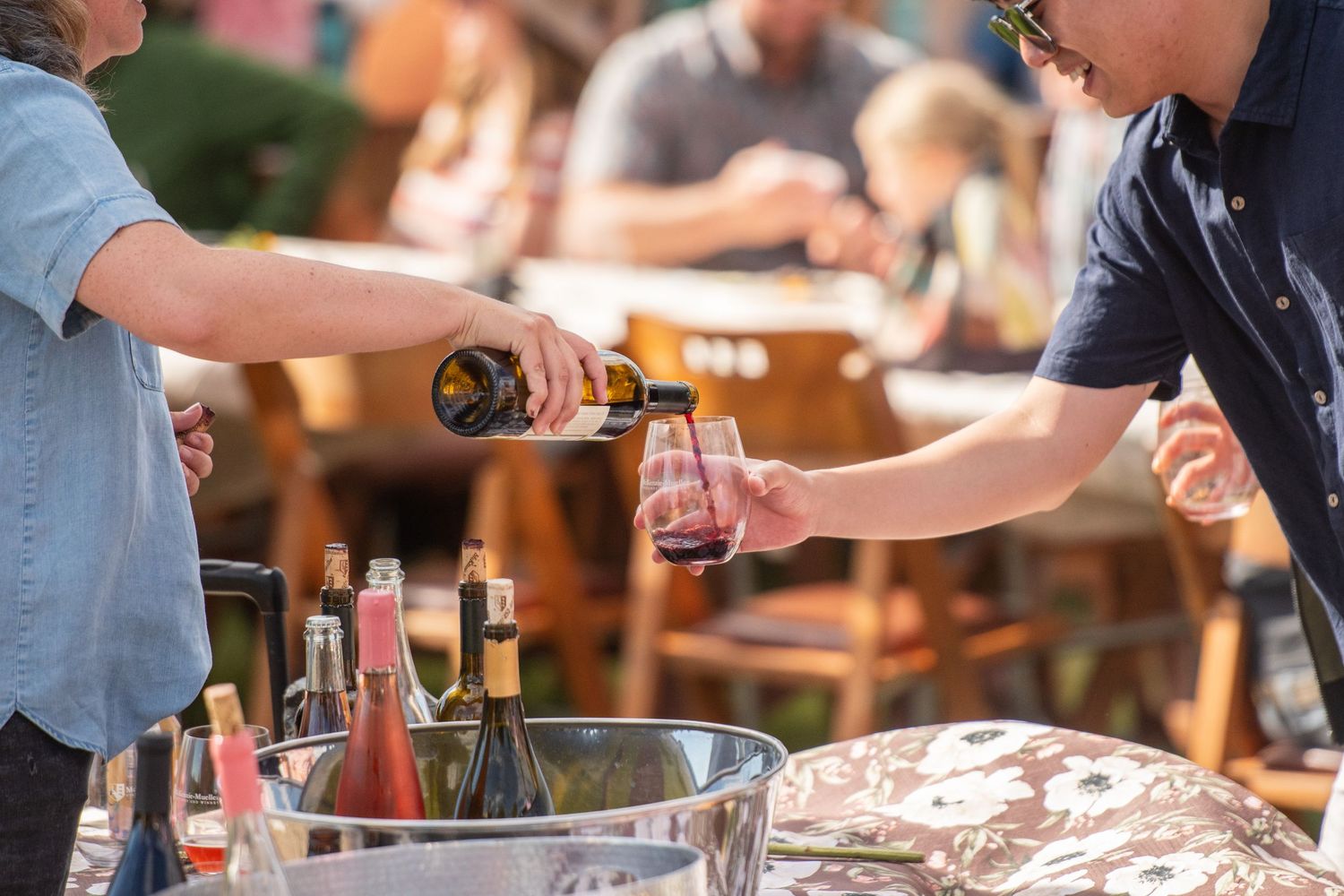 People gathering around a rustic wooden table for wine tasting outdoors.