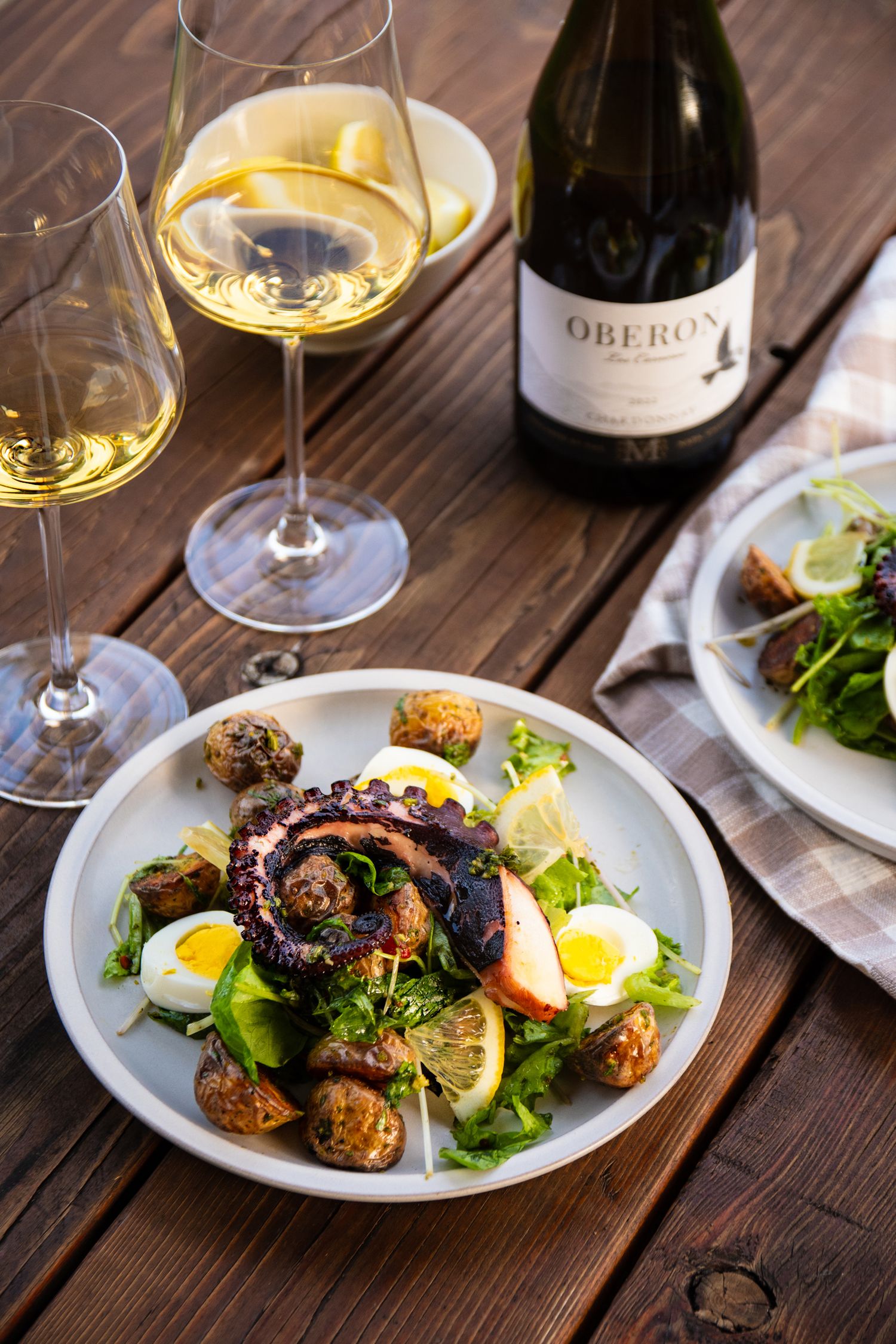 Gourmet meal with eggs, greens and wine served on white plates on rustic wooden table.