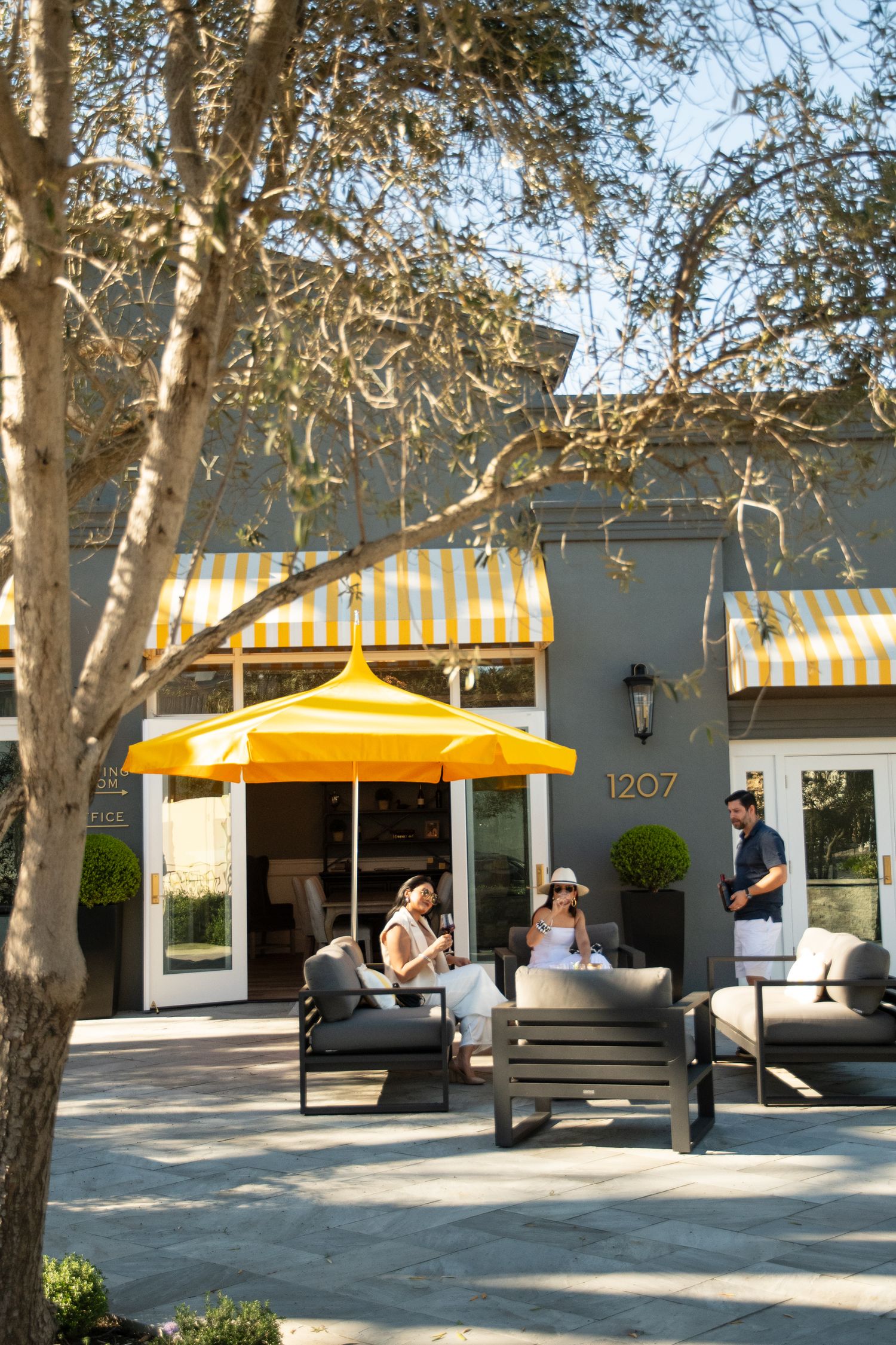 Outdoor patio seating with yellow striped awnings and umbrella at building 1207, guests relaxing on modern furniture.
