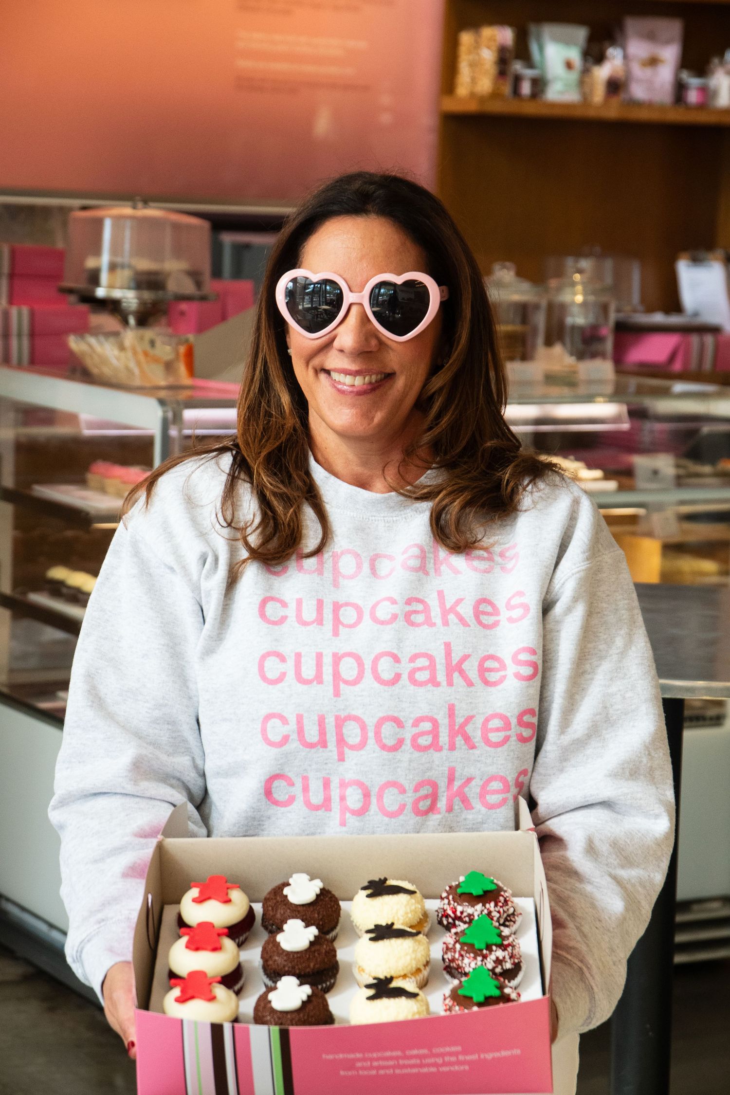 Display of festive holiday cupcakes in decorative box with cupcake-themed sweatshirt.
