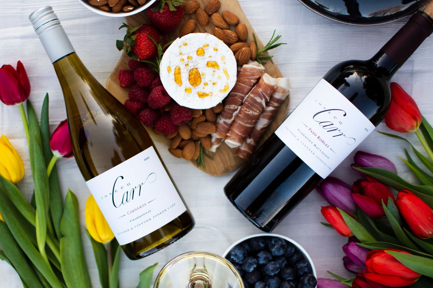 Wine bottles and colorful tulips arranged on a light gray surface with decorative labels.