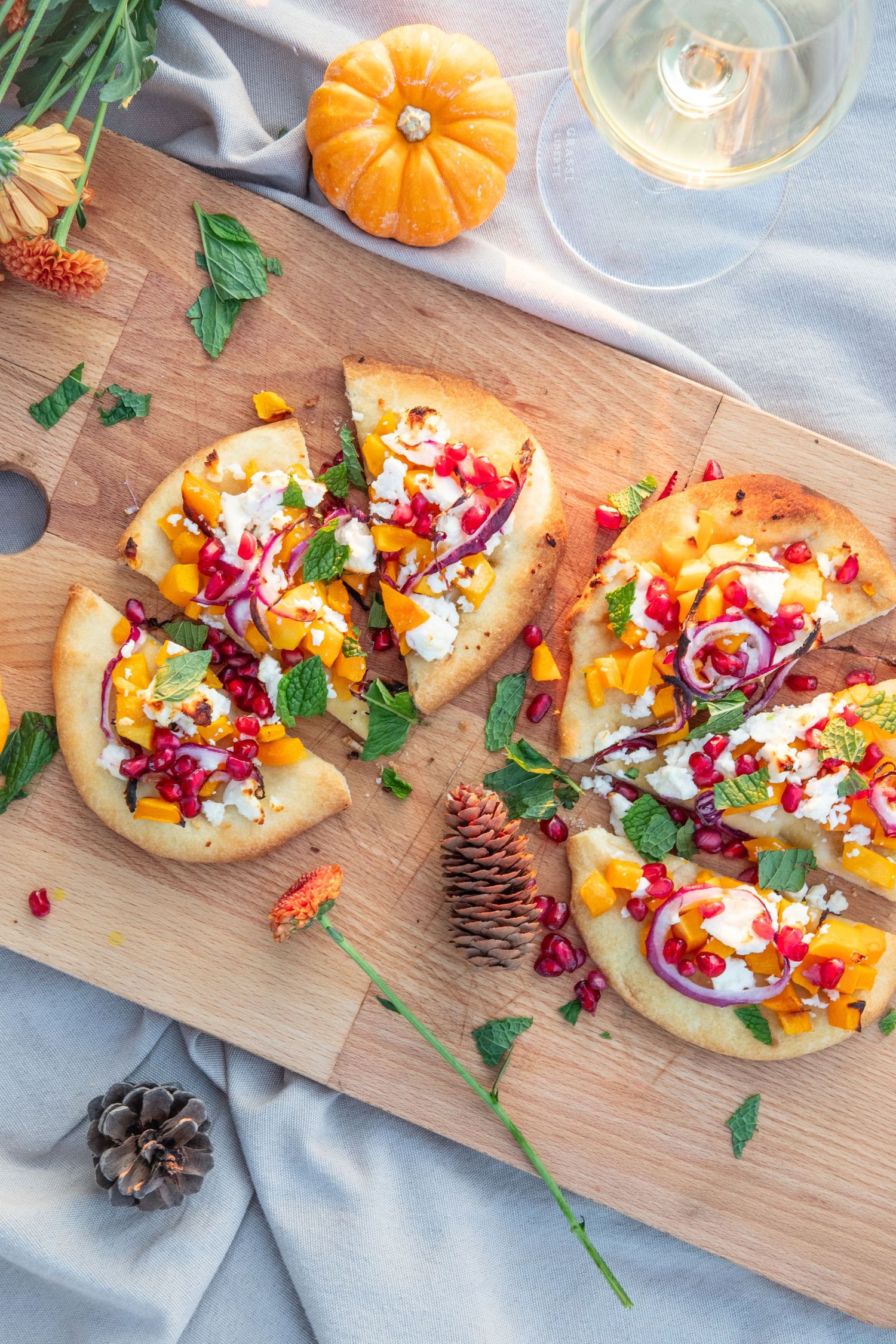 Colorful flatbread appetizers topped with pomegranate seeds and herbs on a wooden serving board.