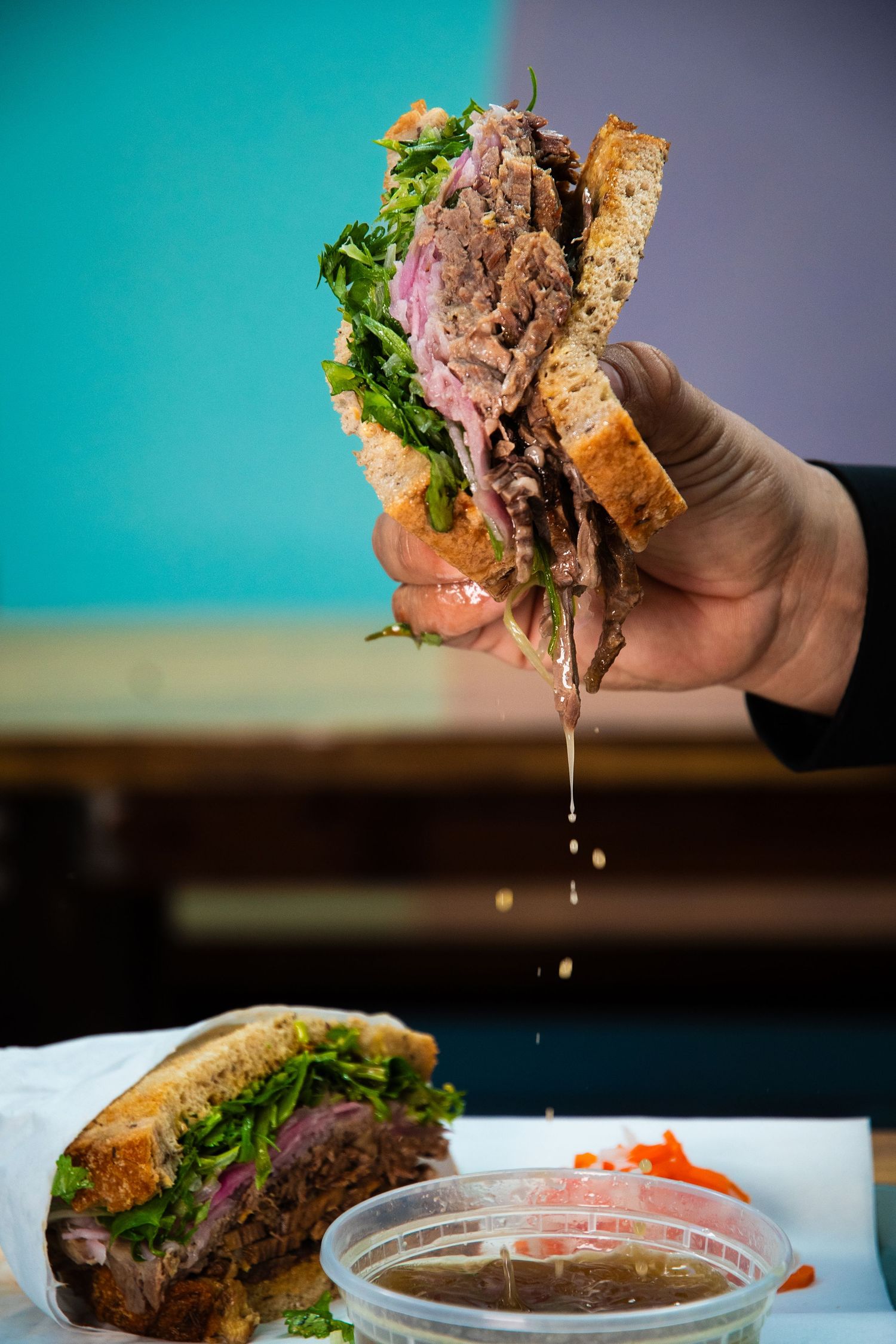 Juicy French dip sandwich dripping au jus sauce over a dipping bowl.