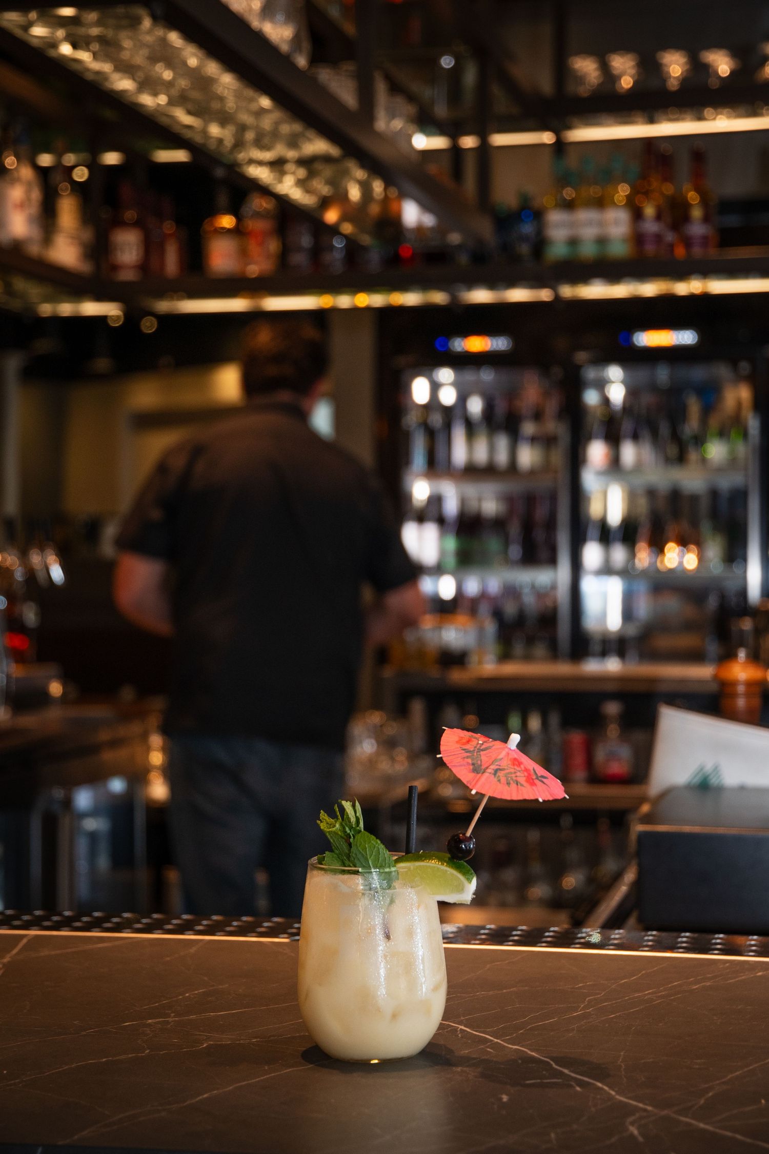 Two tropical cocktails garnished with umbrellas and lime on a dark bar counter.