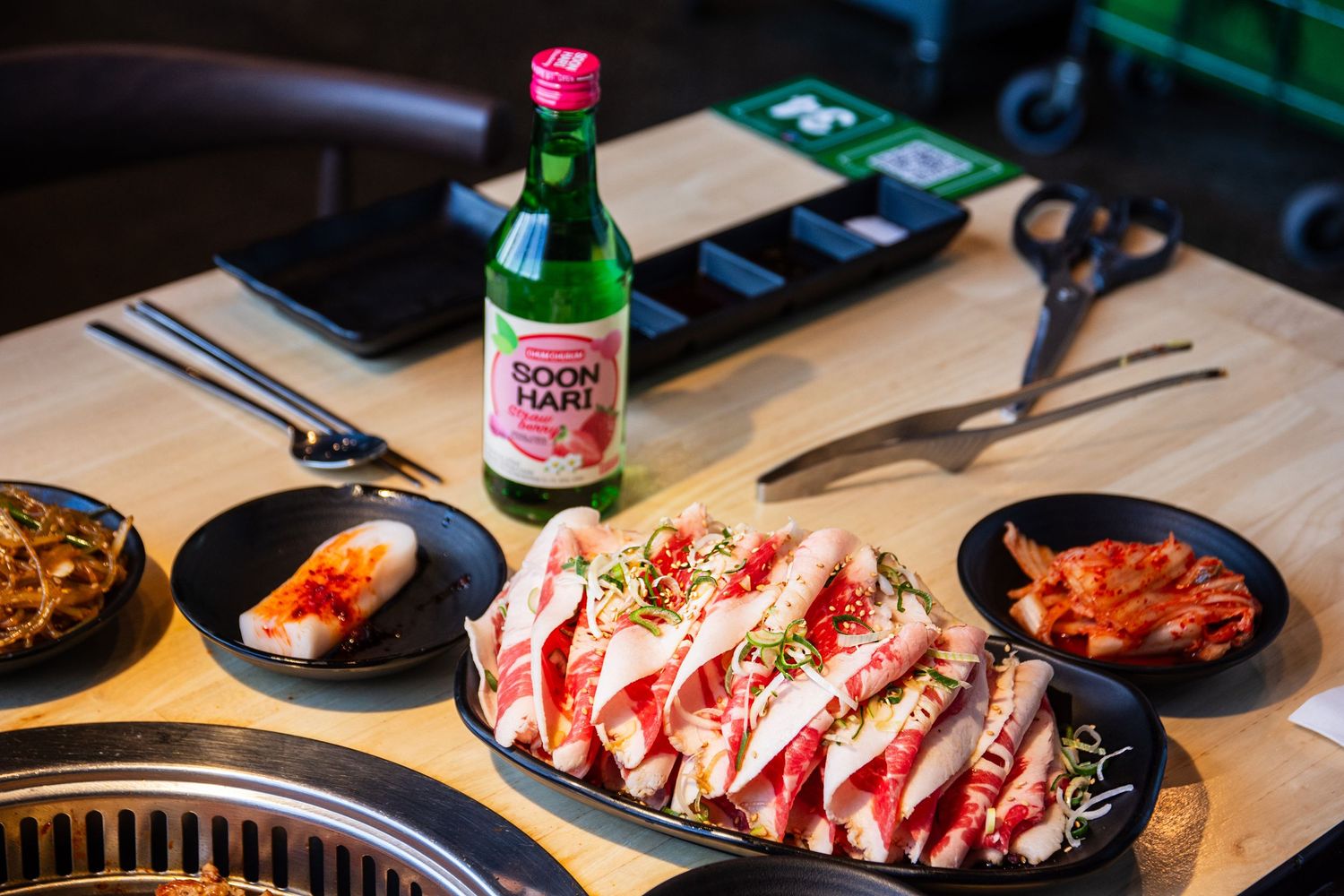 Japanese style meat dishes and beverages arranged on dark table with dramatic lighting.