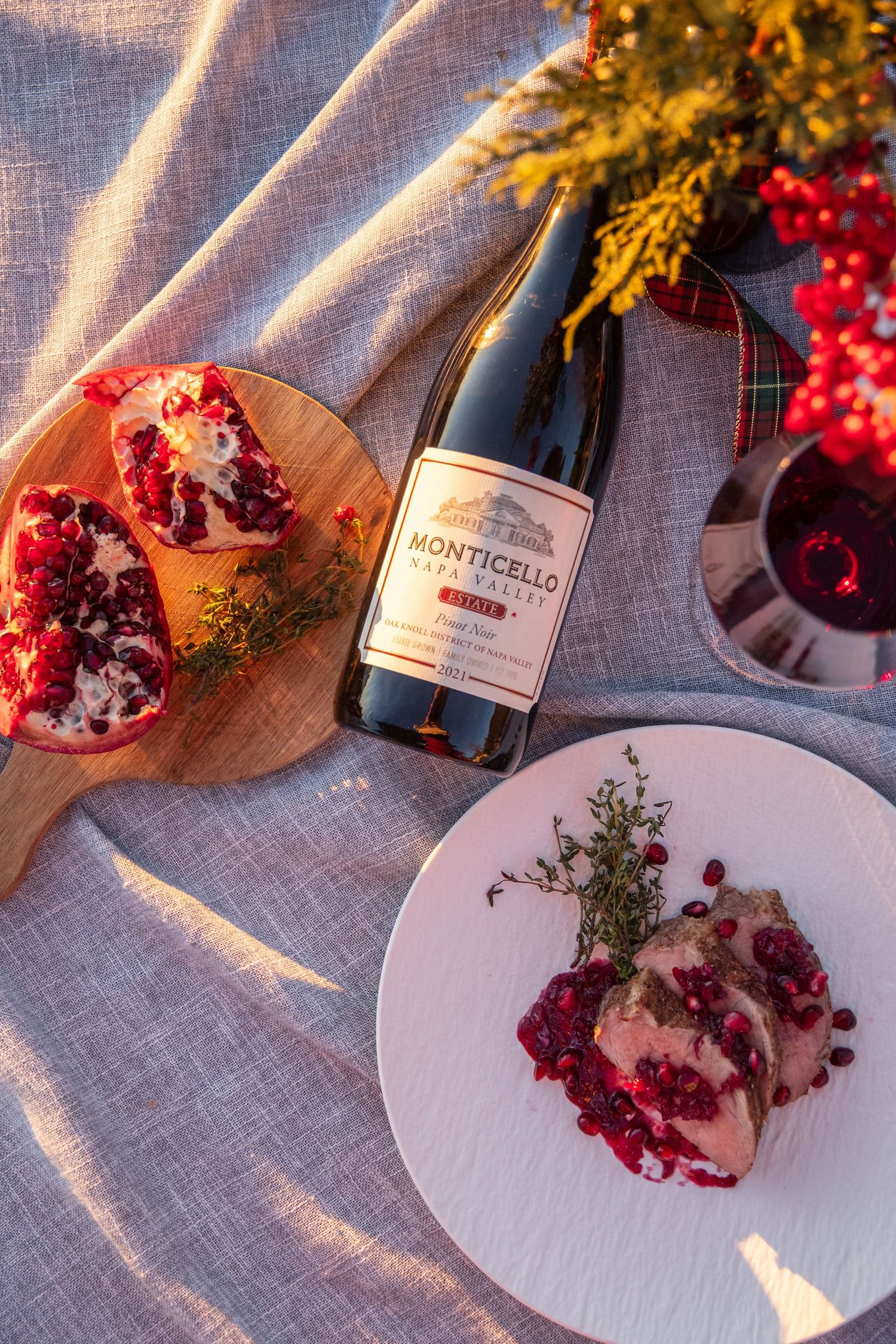 Wine bottle and pomegranate on linen tablecloth with warm lighting and seasonal decorations.