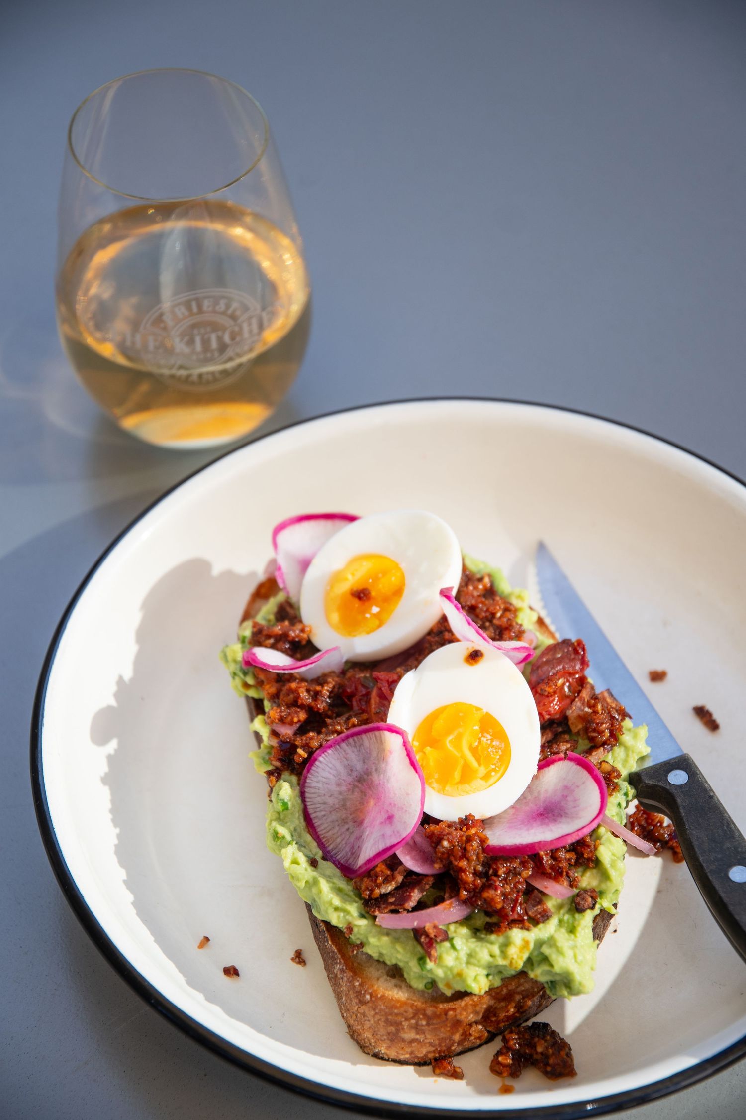 Avocado toast topped with soft boiled egg, radishes and microgreens on an enamel plate.