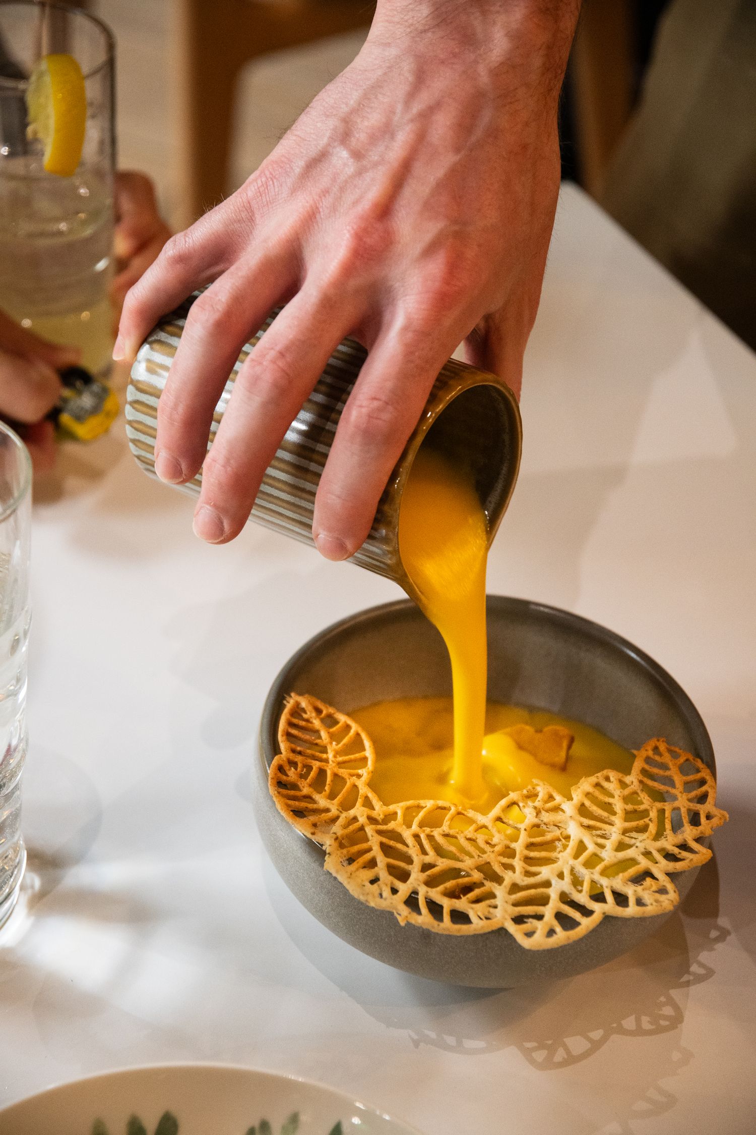 Pouring orange liquid over decorative lattice-shaped garnishes on plates.
