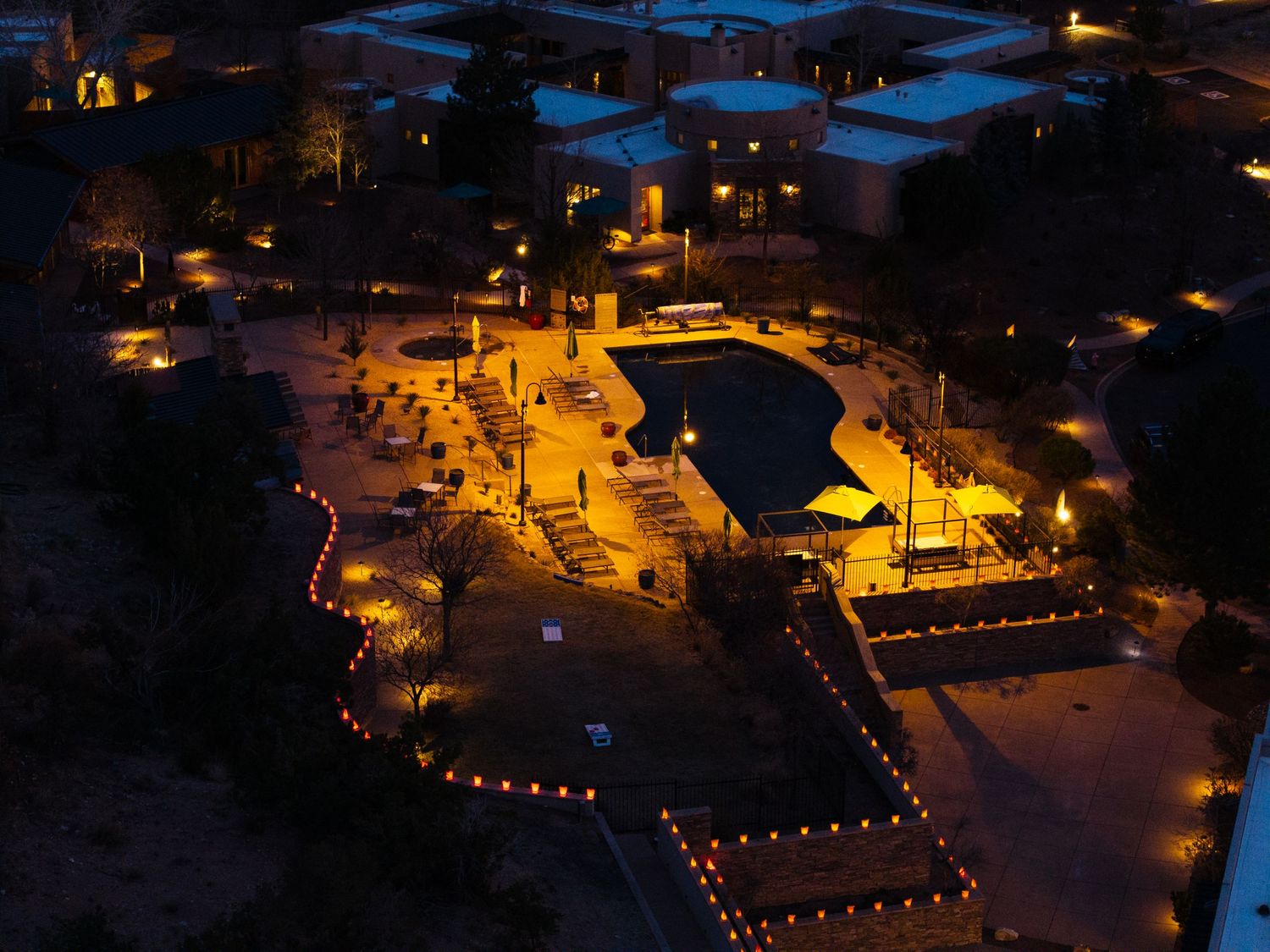 Aerial night view of illuminated resort pool area with warm golden lights outlining pathways and landscaping.