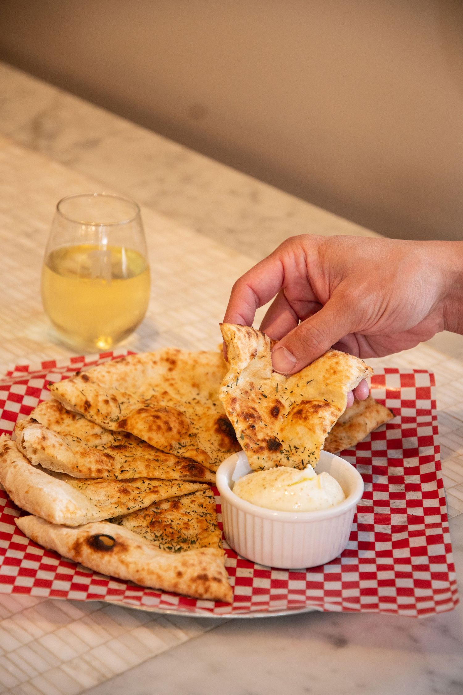Grilled flatbread with dipping sauce served on a red and white checkered paper.