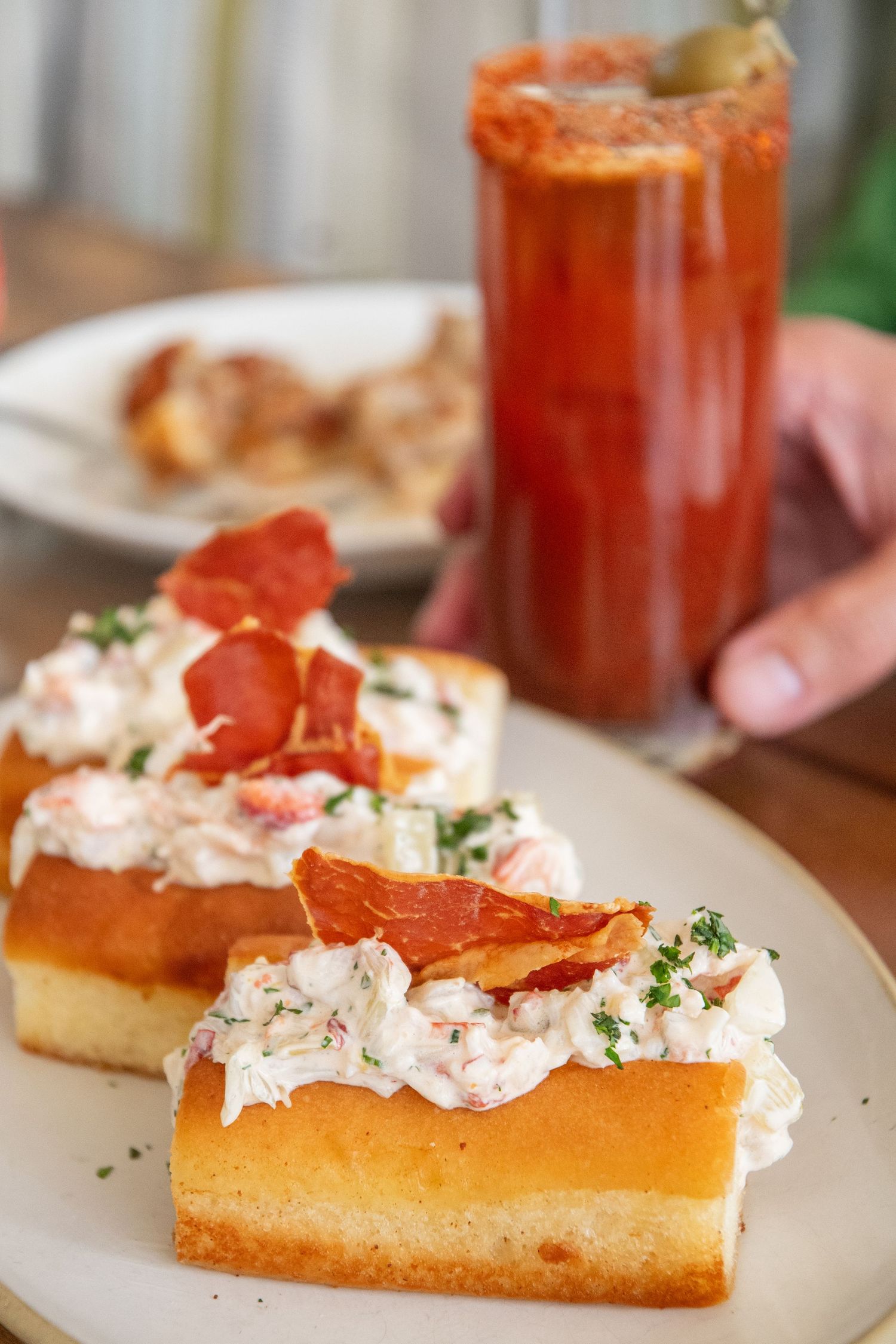 Lobster roll topped with fresh herbs and served alongside a red cocktail.