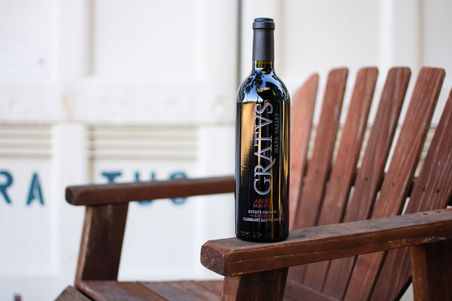 A bottle of Gratus red wine resting on a wooden Adirondack chair outdoors.