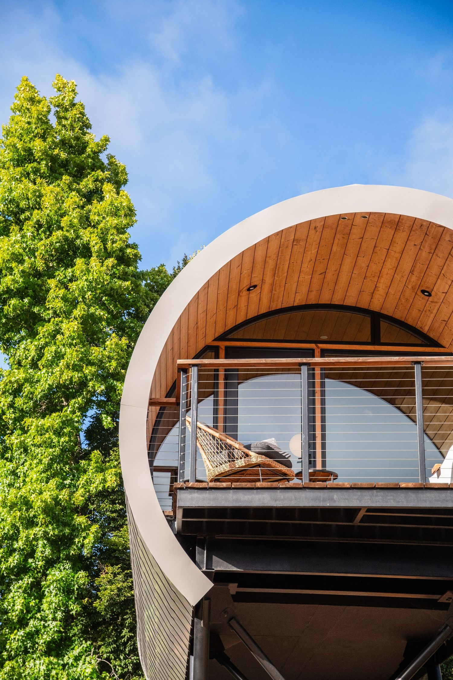 Modern curved architectural structure with metal railings against bright green foliage.