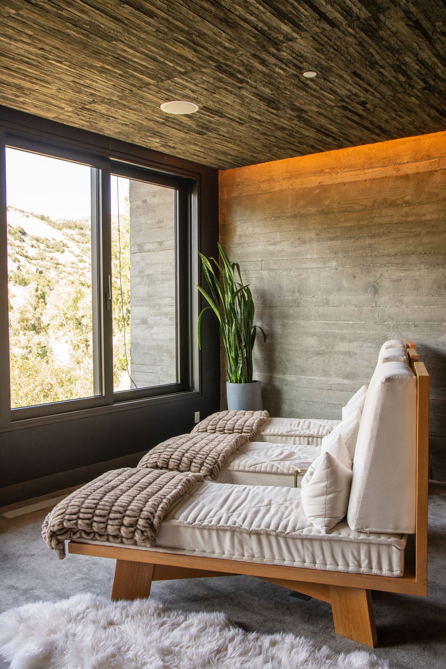 Modern daybed with chunky knit pillows next to large window overlooking mountain landscape.