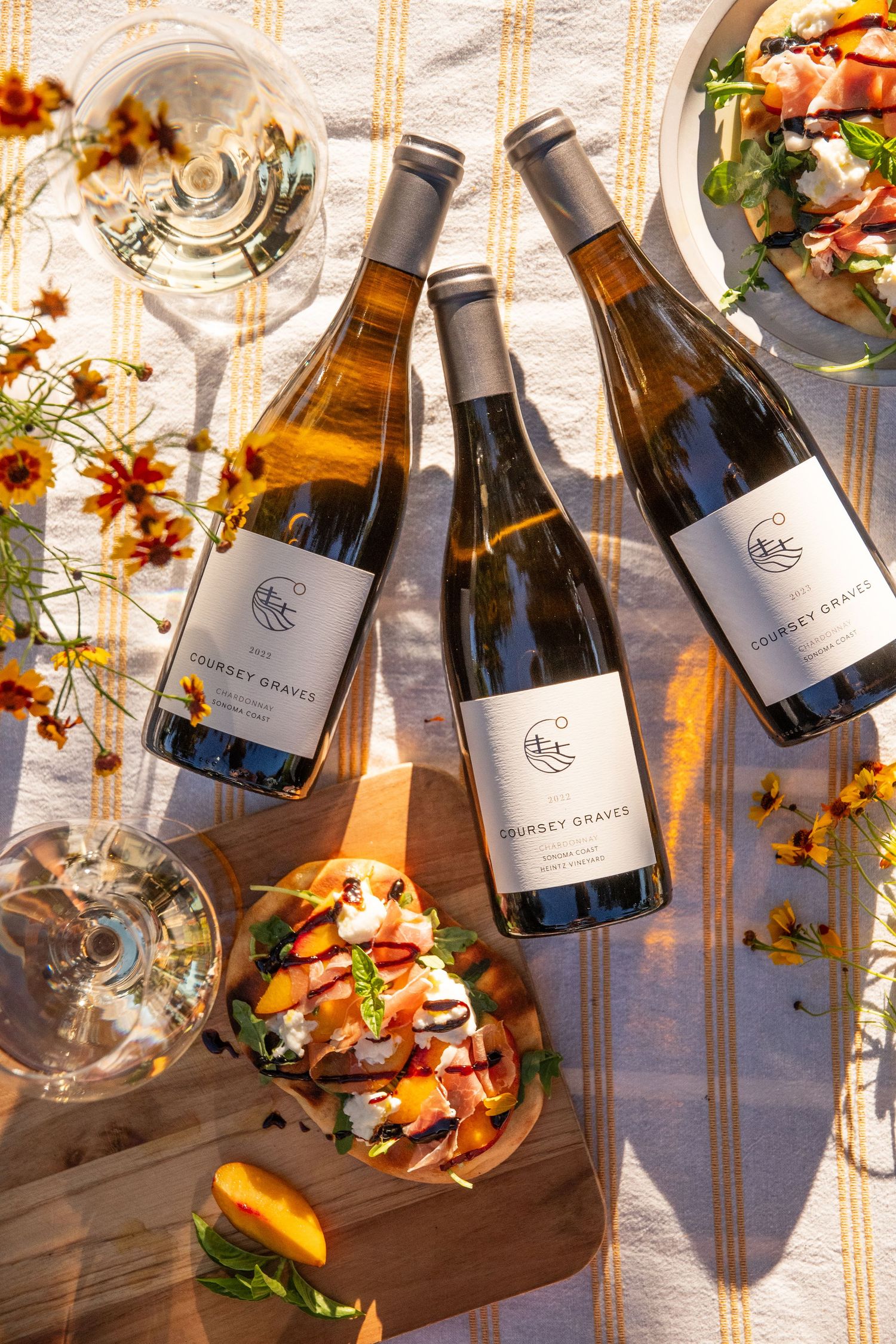 Wine bottles and glasses arranged artfully with autumn leaves on a rustic wooden surface in natural lighting.