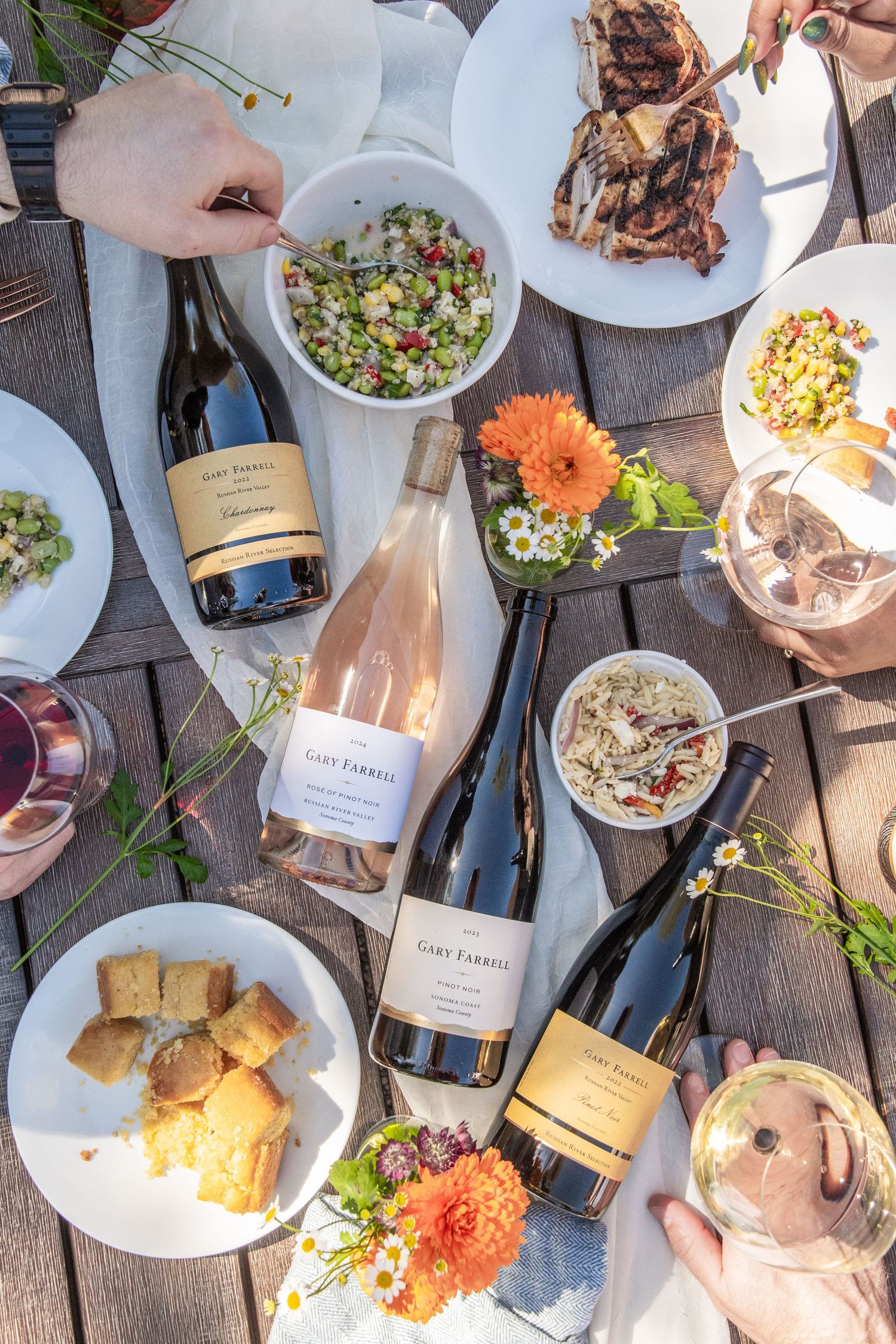 Overhead view of an outdoor dining spread with wine bottles and appetizer plates on a wooden deck.