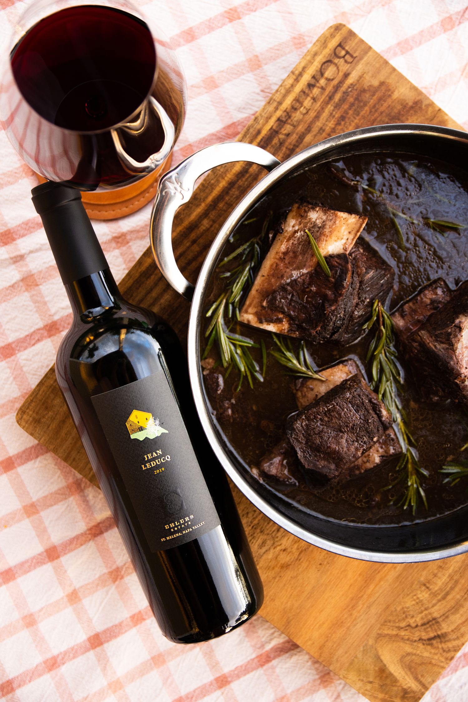 Dark braised meat dish served with red wine and herbs on rustic wooden board.