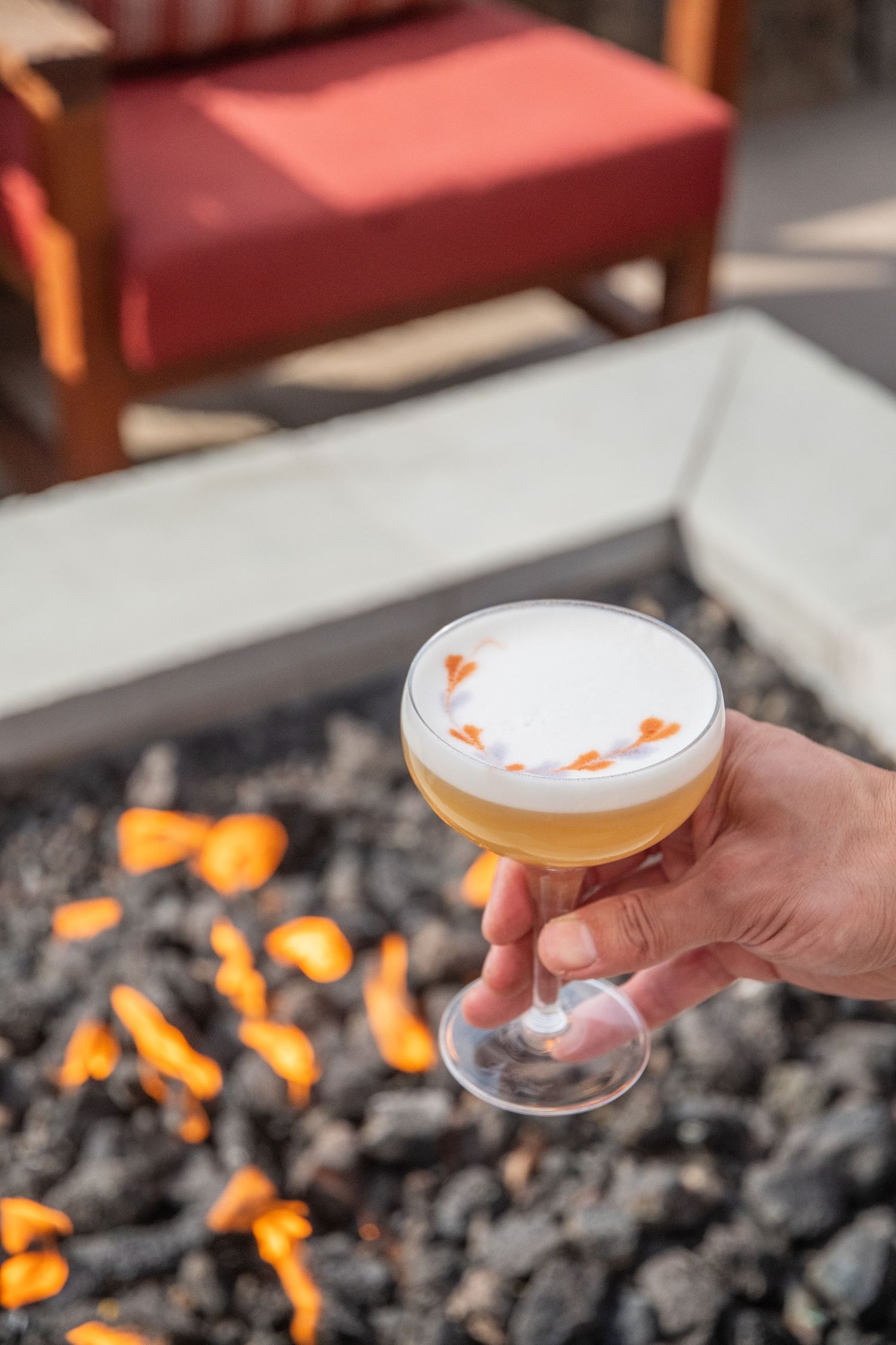 Cocktail glass held over an outdoor fire pit with glowing embers.