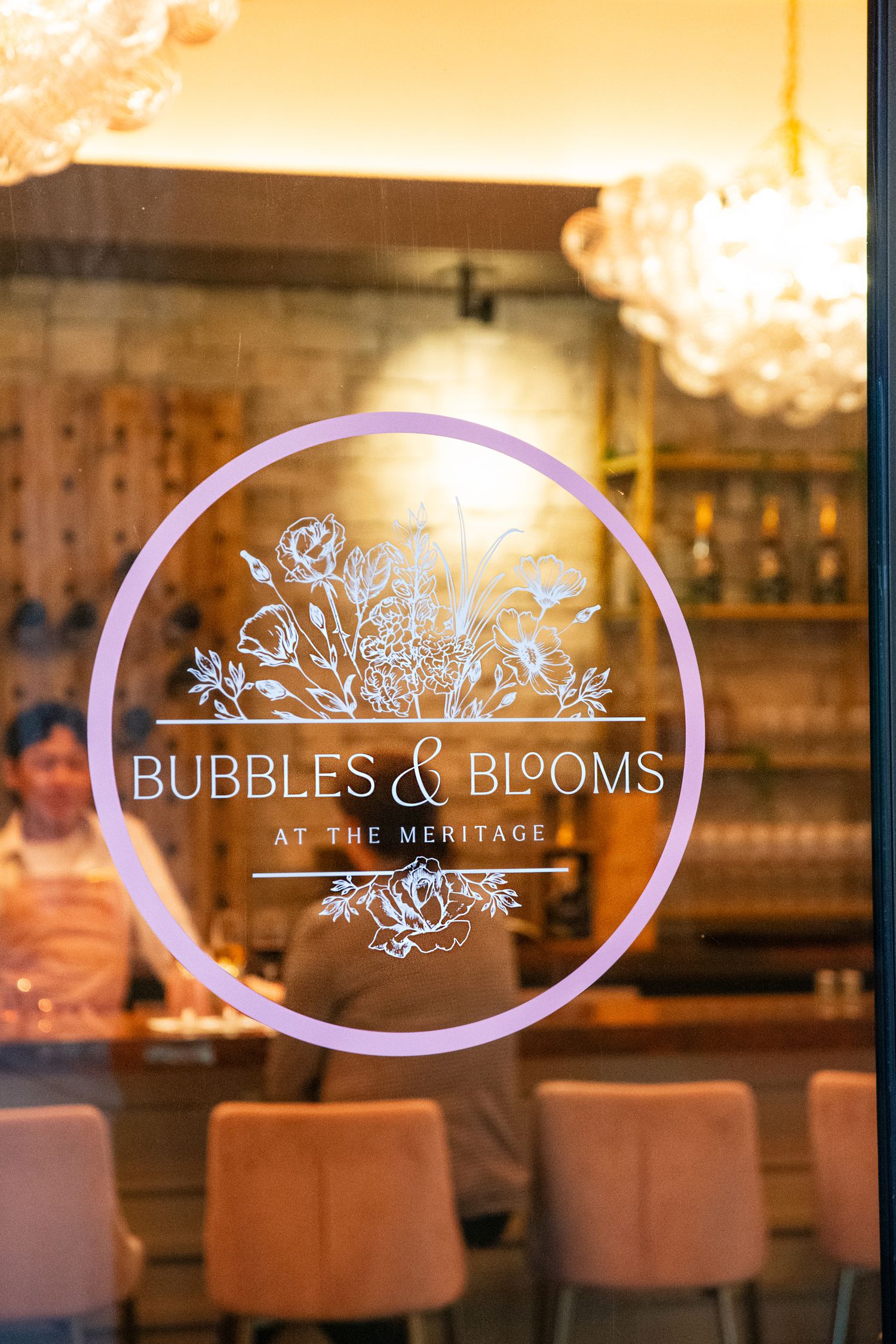 Elegant illuminated Bubbles & Blooms logo sign with crystal chandeliers in an upscale restaurant setting.