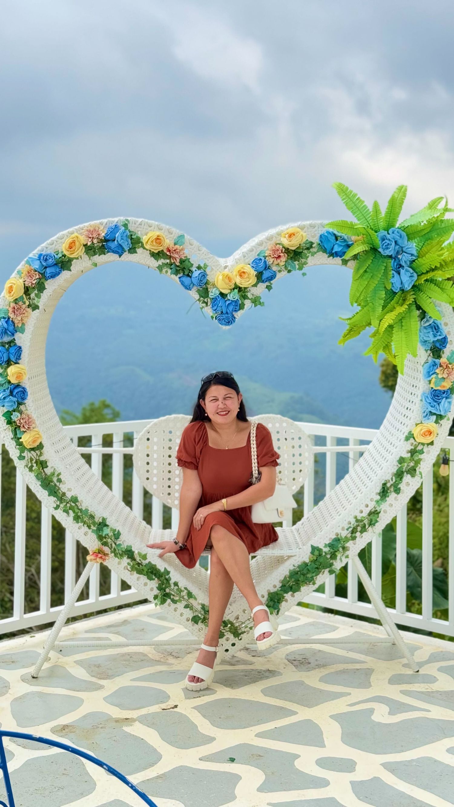 White balcony decorated with blue and yellow flowers and palm leaf decorations overlooking ocean view.